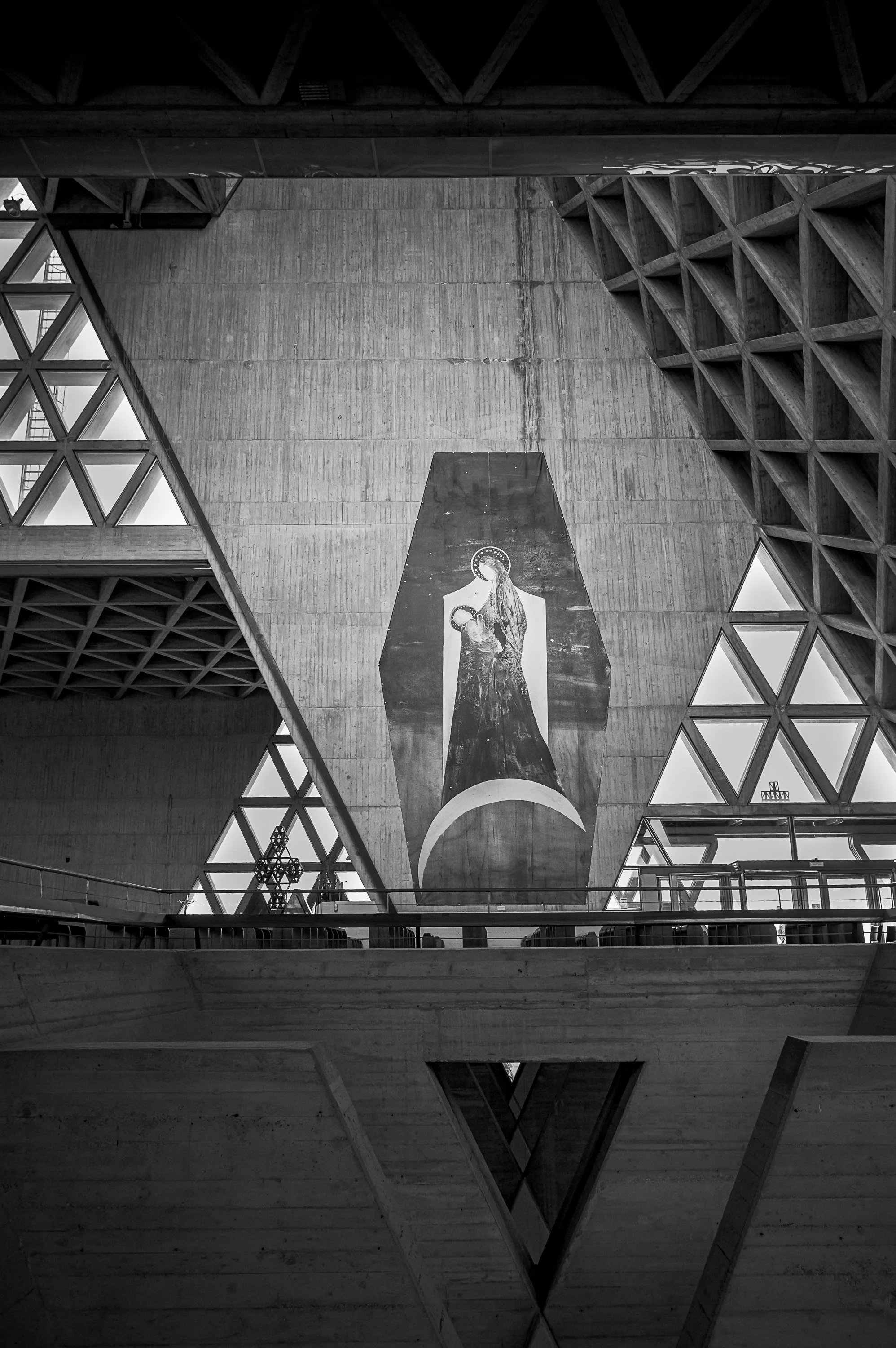 Religious wall image framed by triangular windows and massive concrete forms.