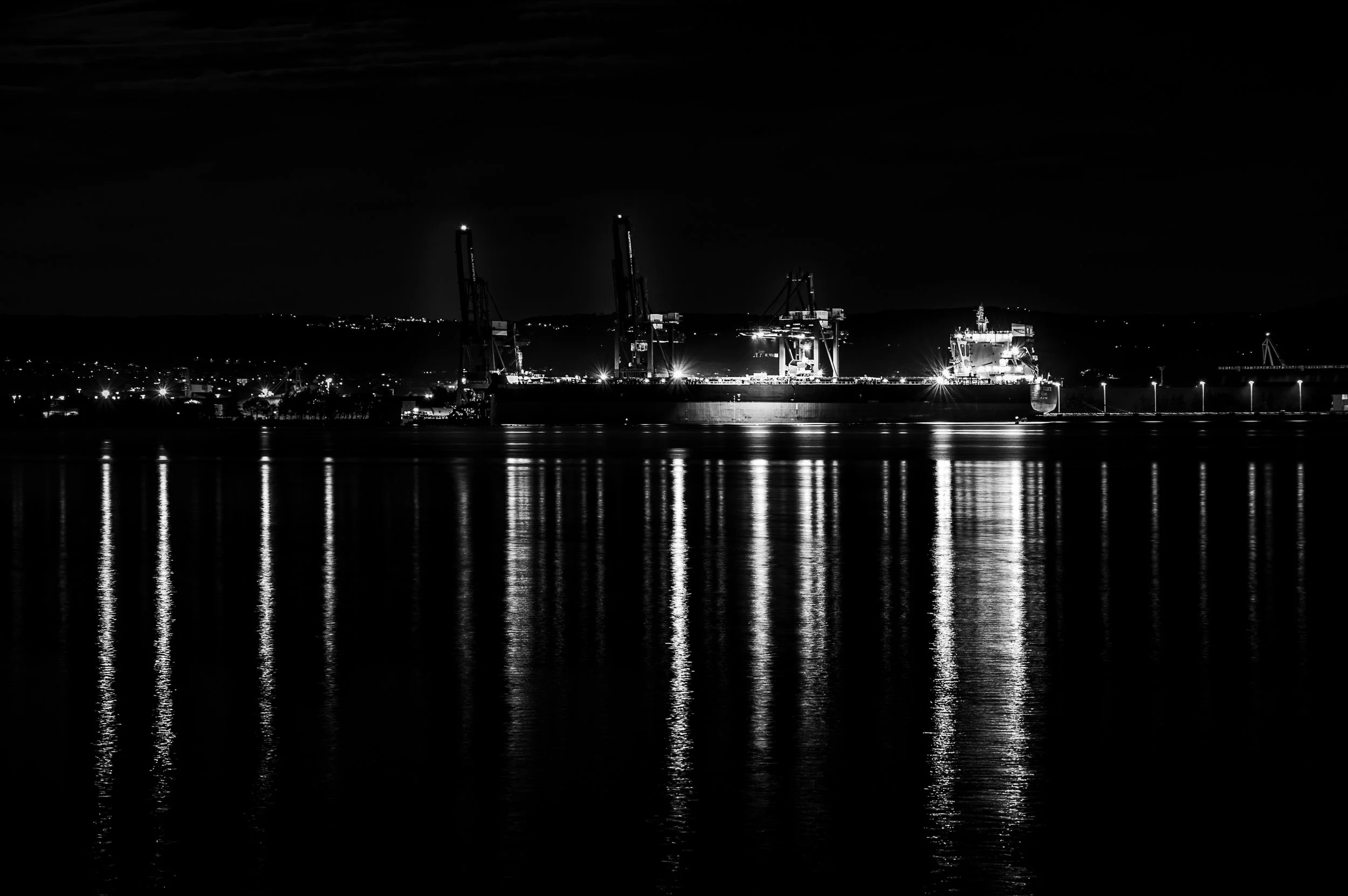 Harbour lights reflected across calm water at night. Opens the After Light series.