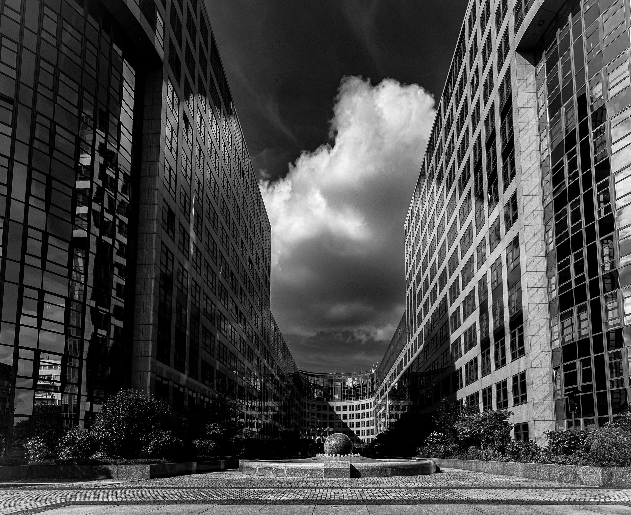 Large cloud framed by symmetrical glass office facades and a central courtyard.