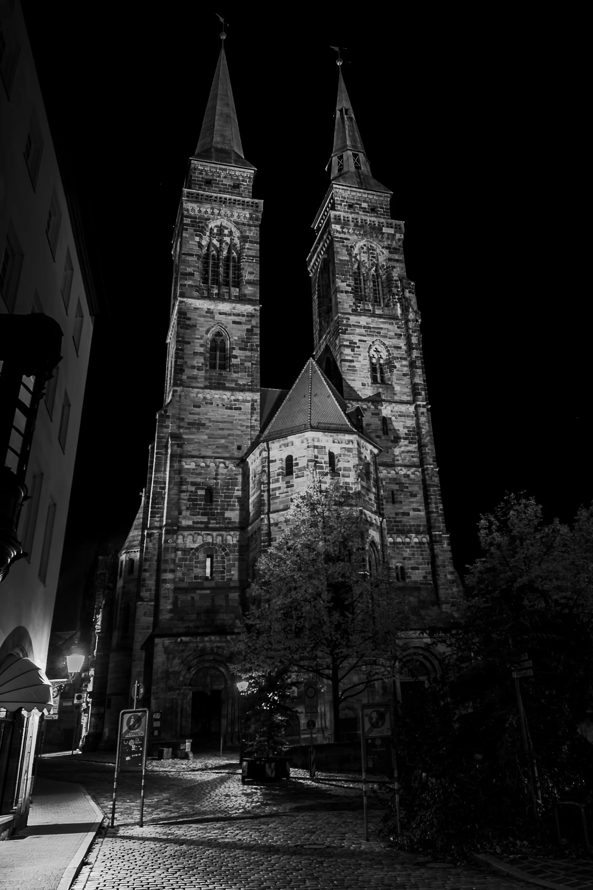 Illuminated twin towers of St. Sebald above wet cobblestones in Nuremberg at night.