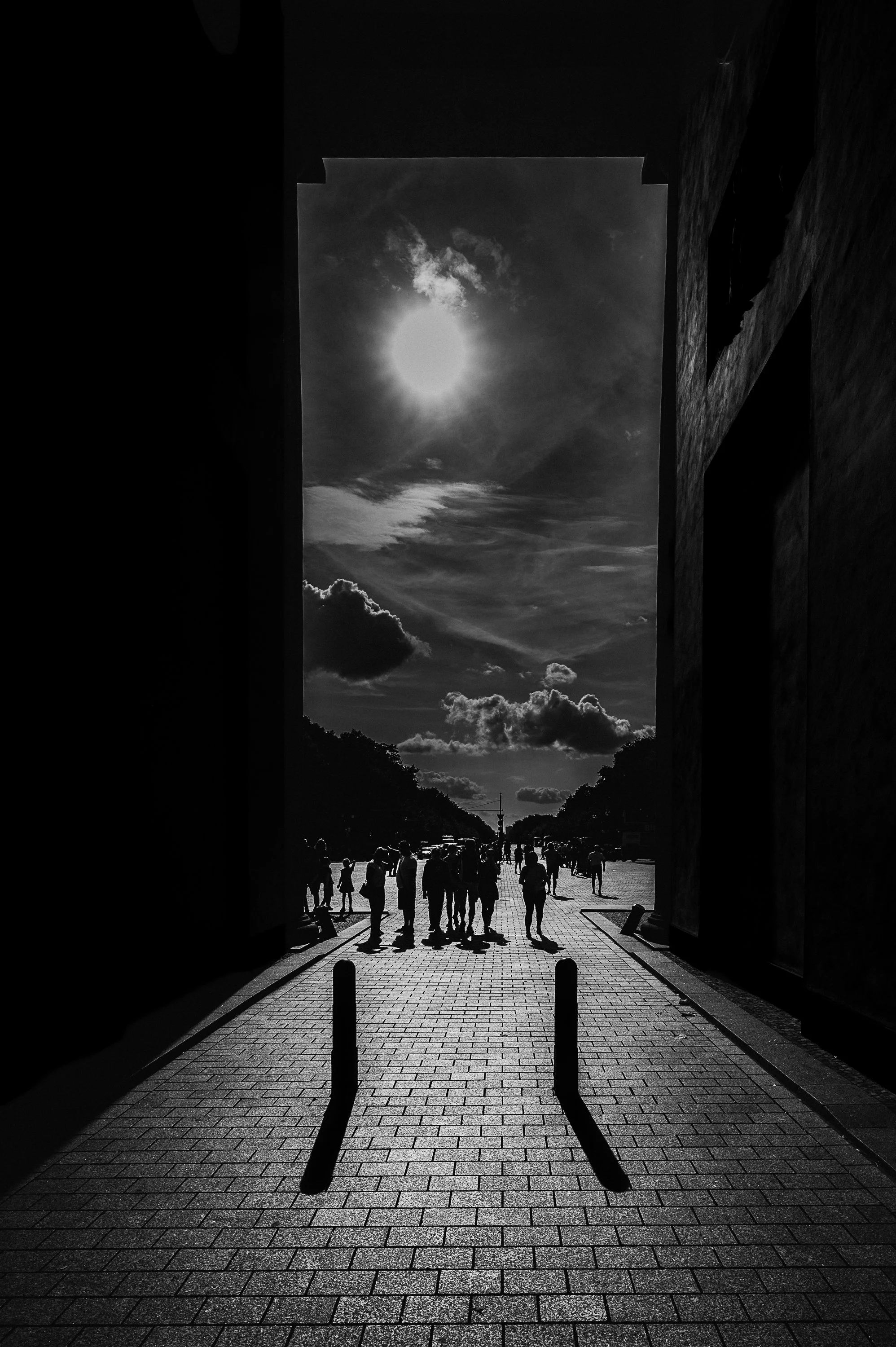 Backlit pedestrians and long shadows seen through the Brandenburg Gate in Berlin.