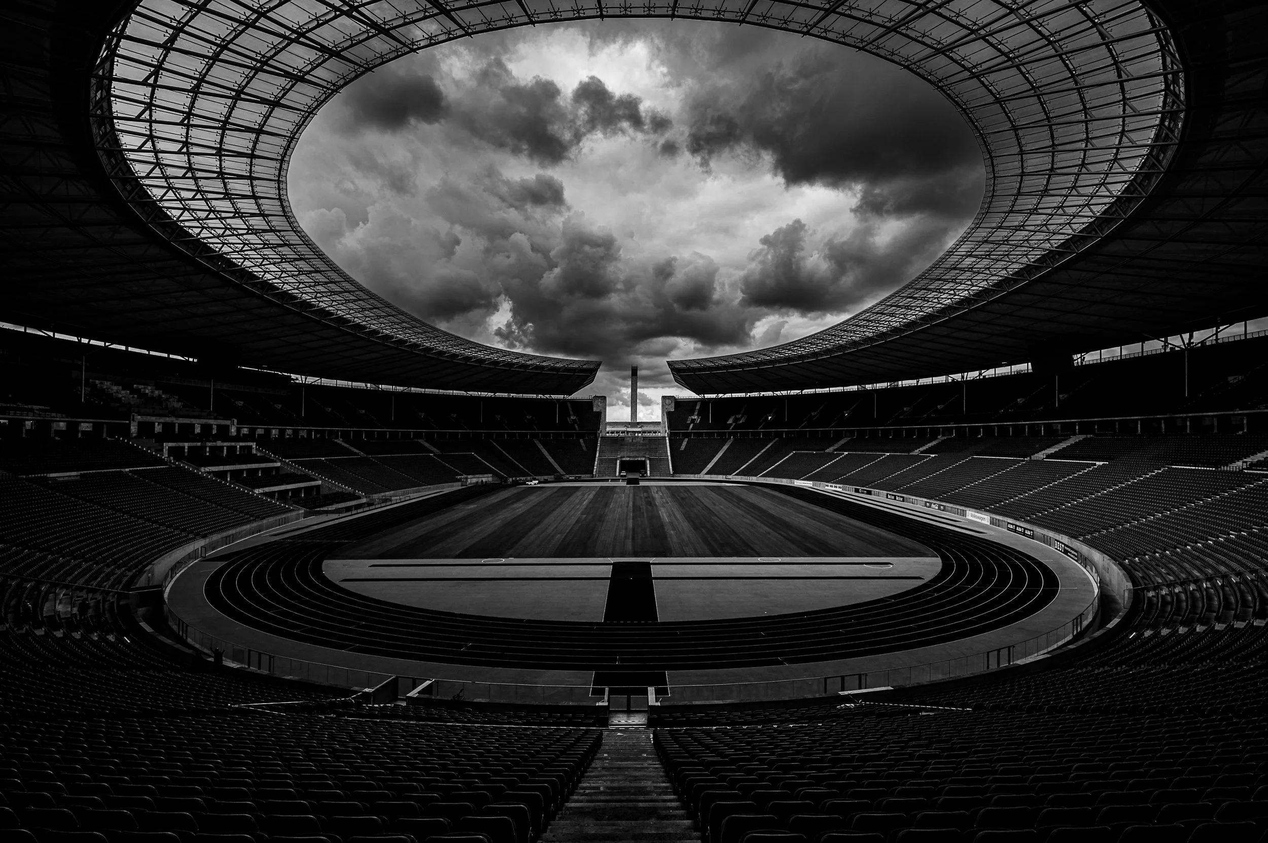 Empty Berlin Olympic Stadium beneath dramatic clouds, seen symmetrically in black and white.