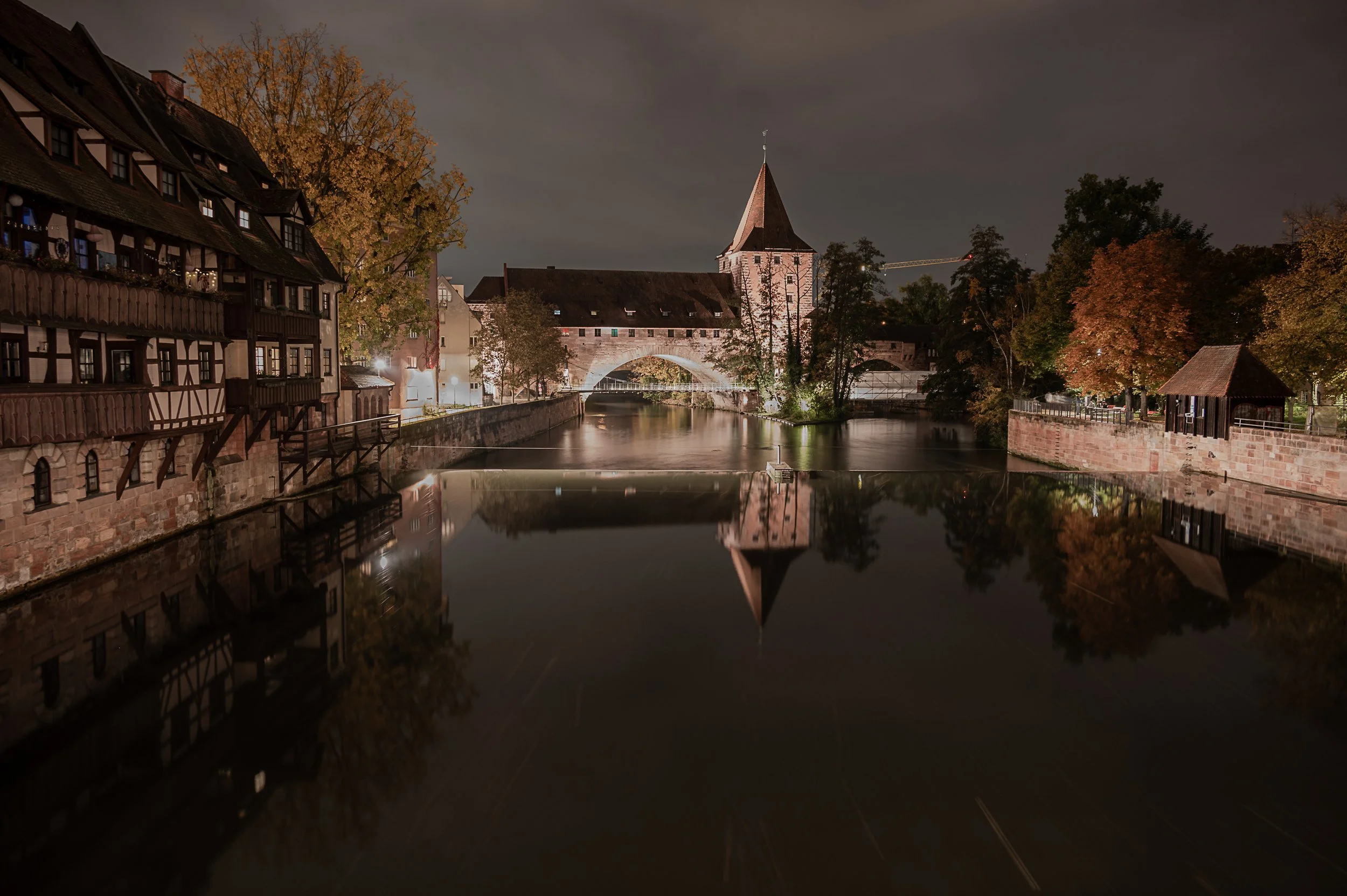Historic bridges and half-timbered houses reflected in calm water in Nuremberg at night.