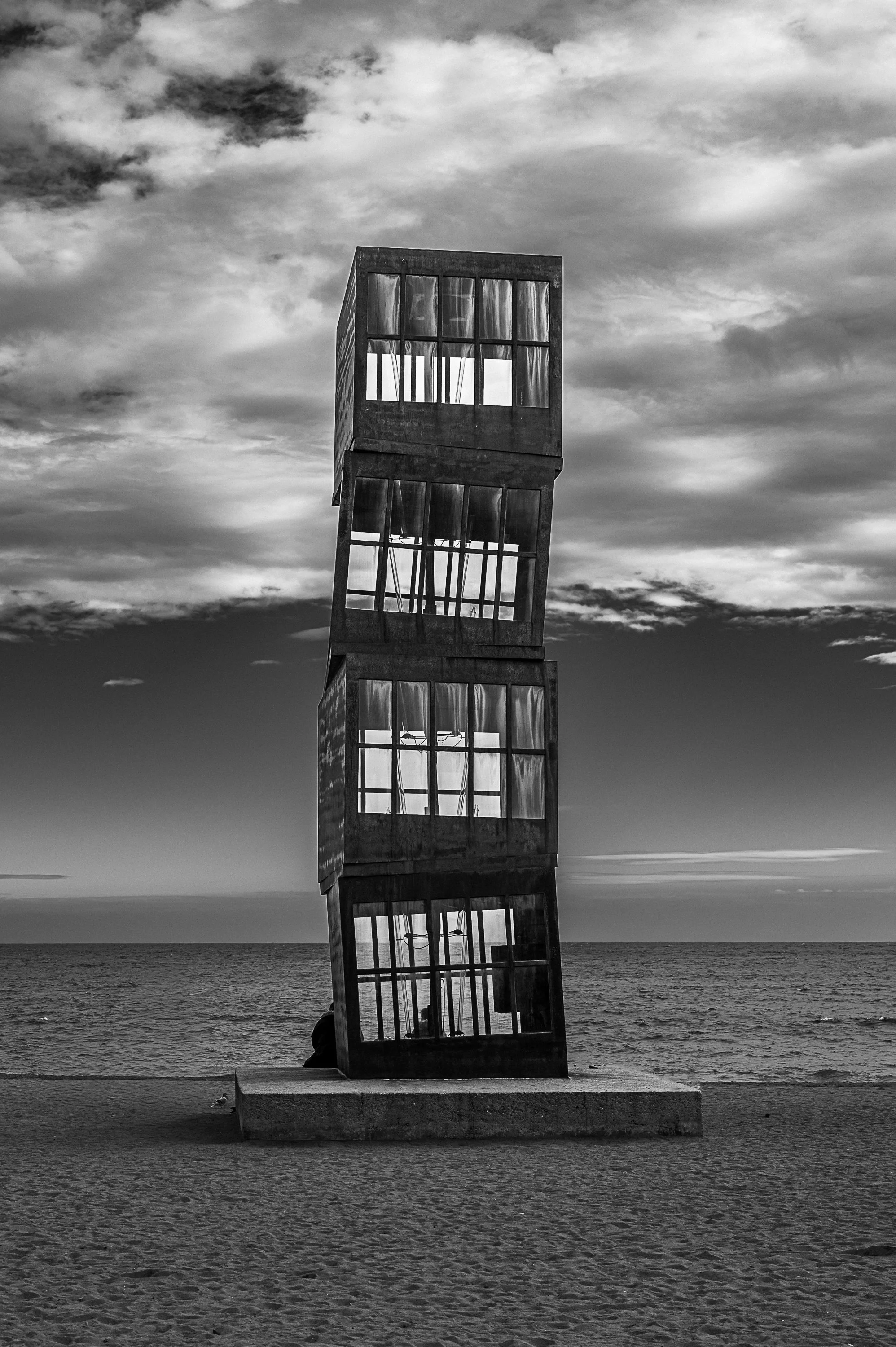 L’Estel Ferit sculpture rising above Barceloneta beach beneath a cloudy sky.