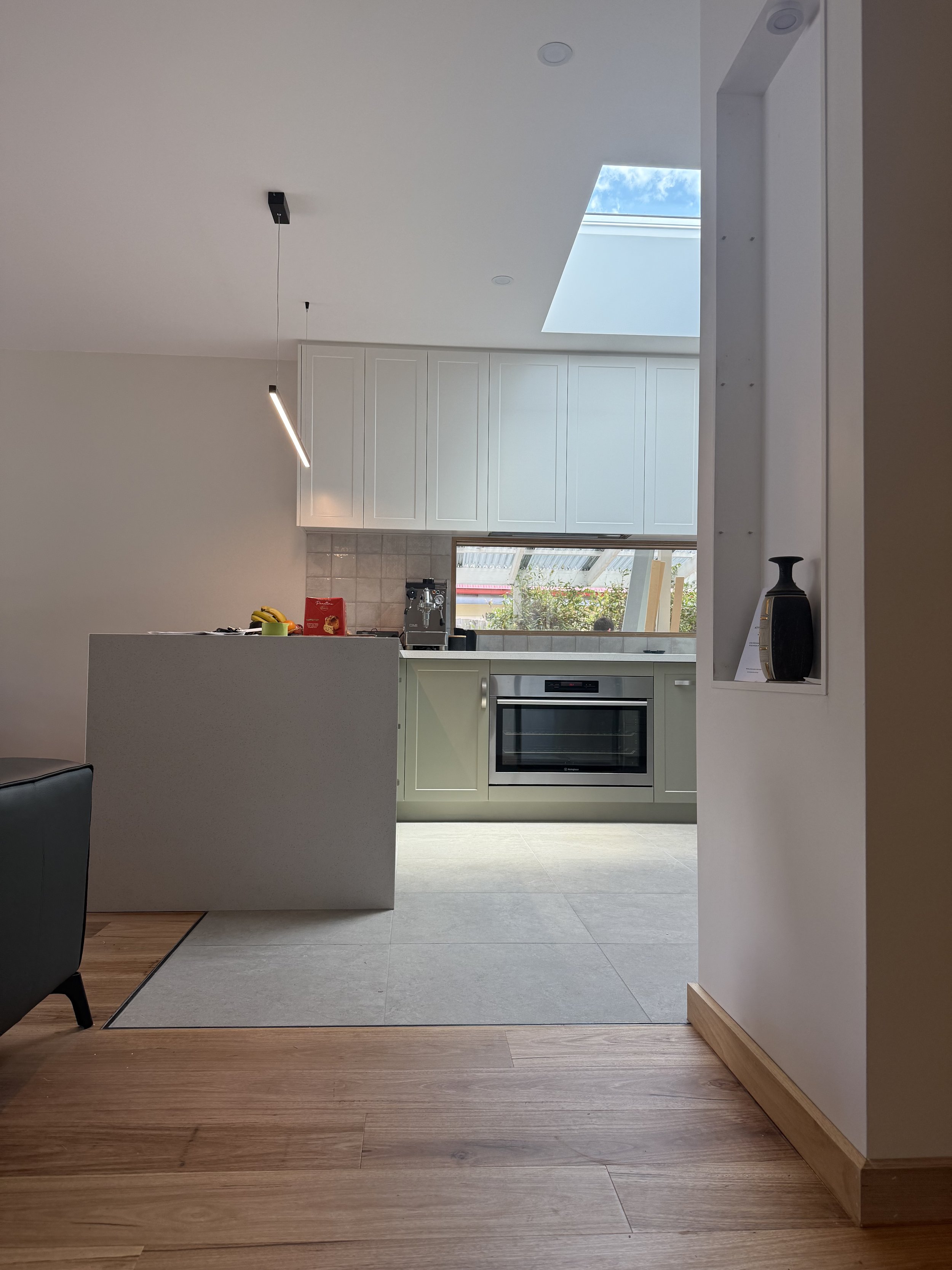 Modern kitchen with white cabinets, a skylight, and a view of the outdoors through a window.