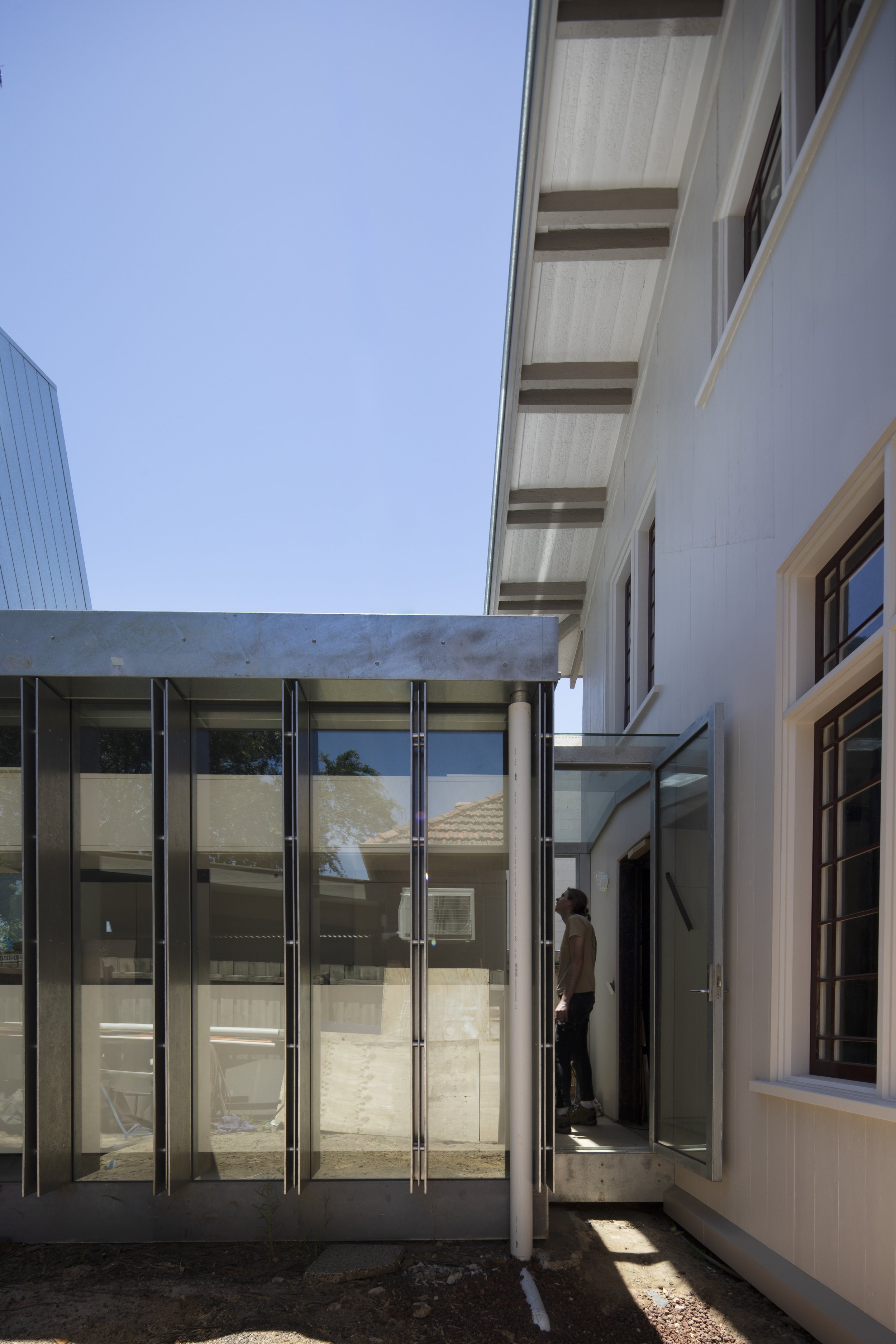 A person standing outside a building near a glass enclosure, with a modern architecture style, under a clear blue sky.