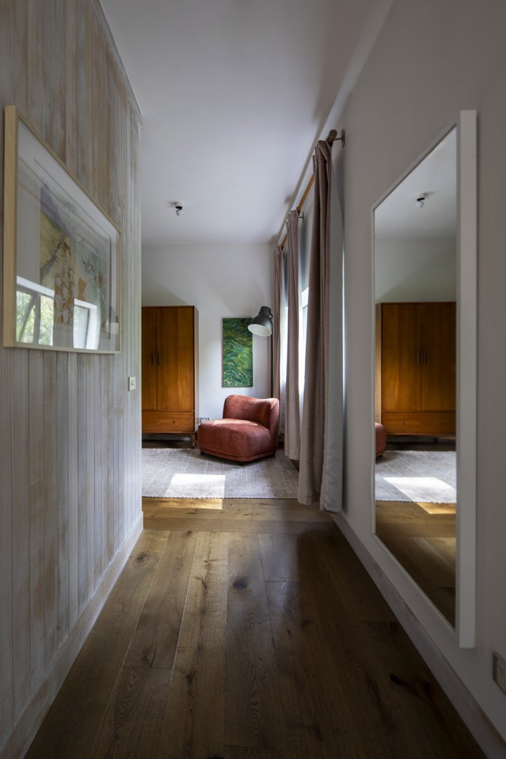 A cozy corner of a room with an armchair, floor lamp, wooden closet, and artwork, reflected in a large mirror.