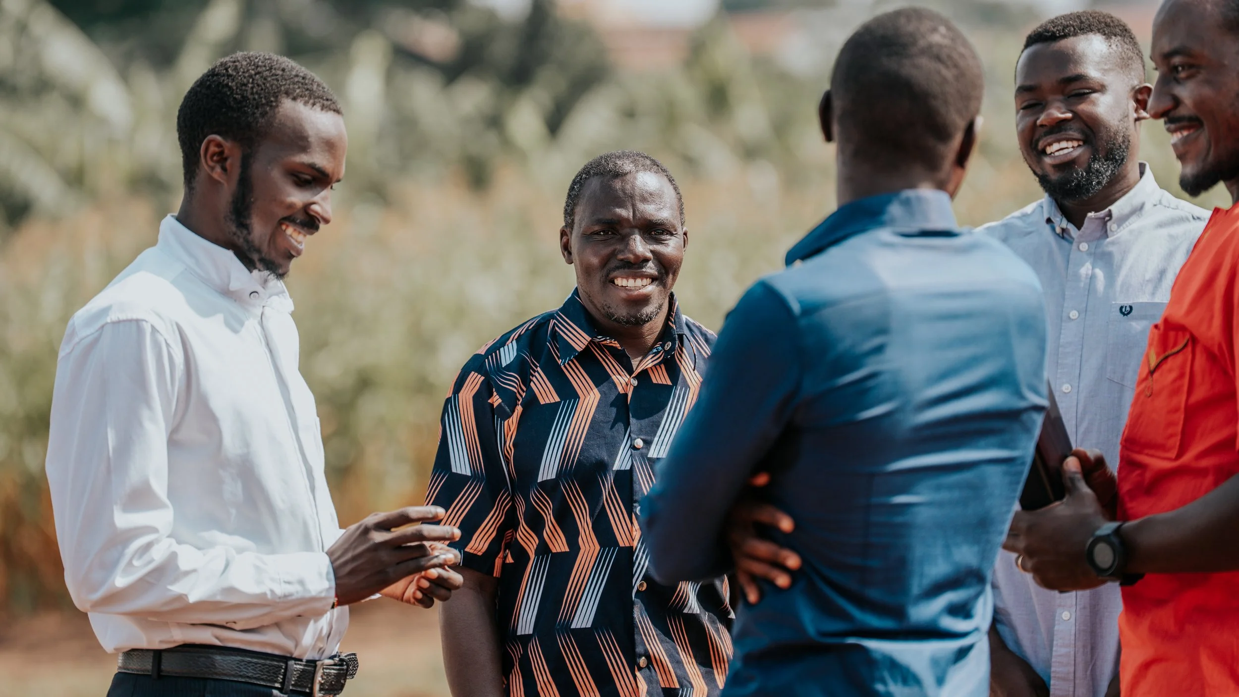 Five men standing outdoors in a semi-circle, engaged in conversation and smiling.