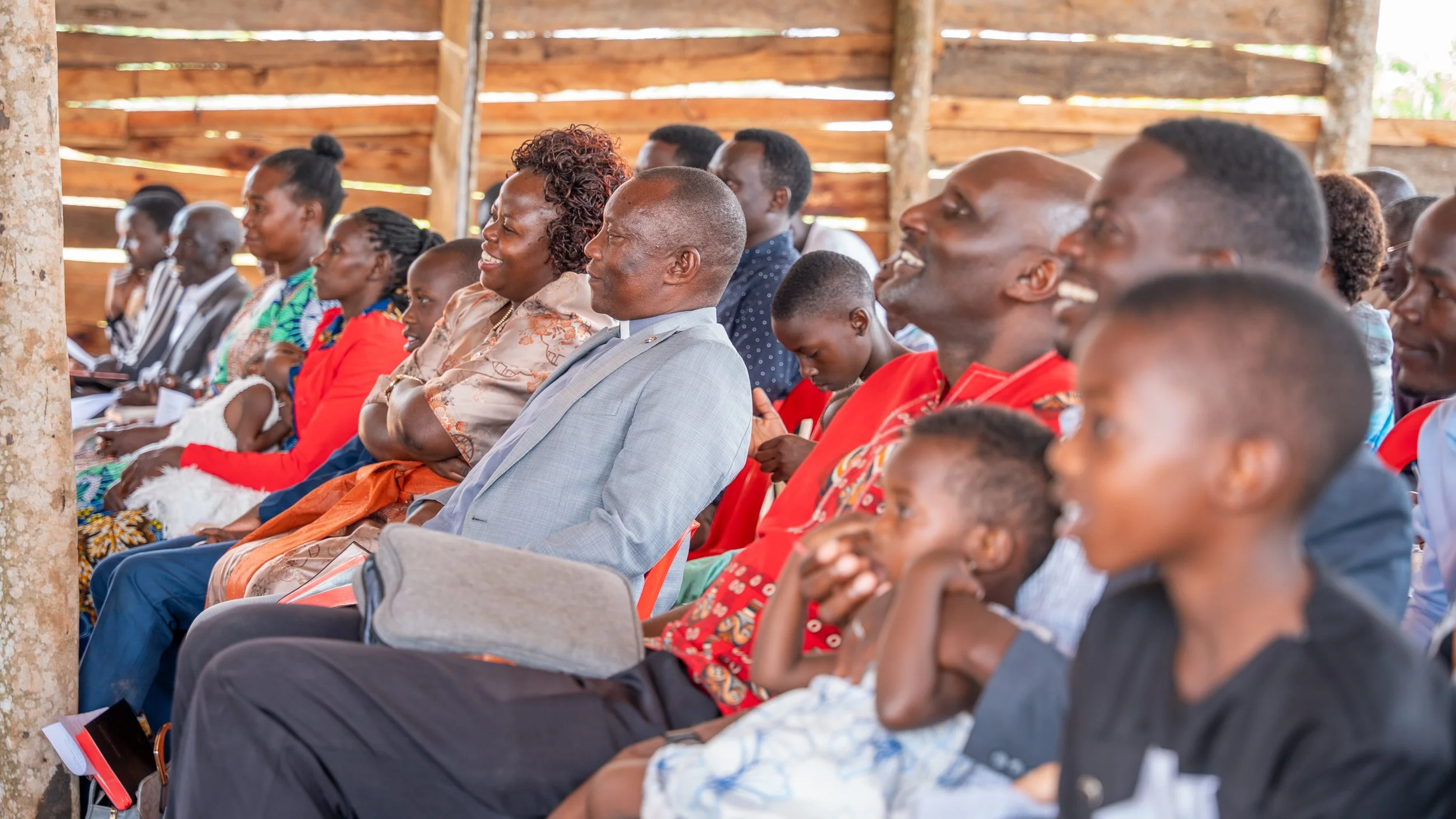 People seated and smiling inside a wooden structure during an event or gathering.