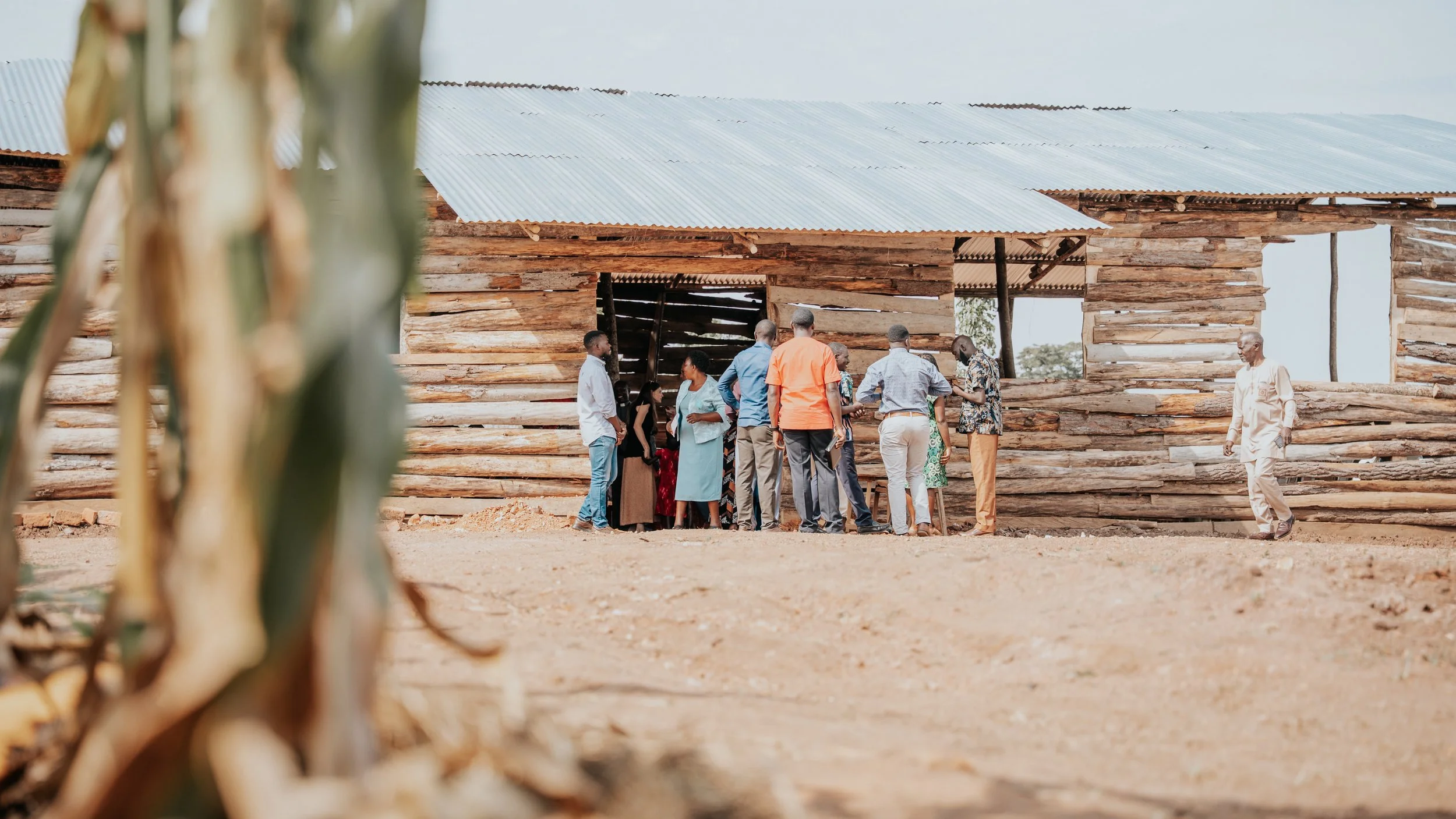 A group of people gathered outside a wooden building with a corrugated metal roof.