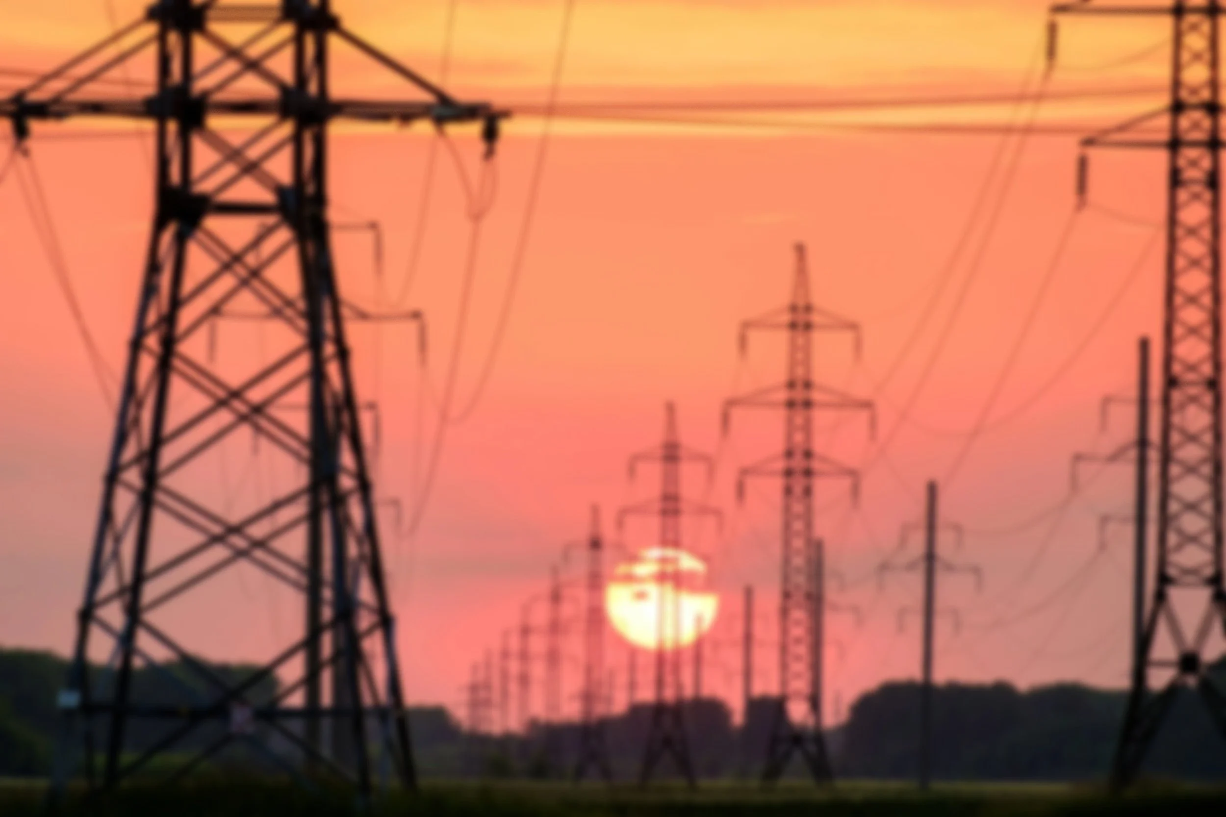 Silhouettes of power lines and electric towers at sunset with a pink and orange sky.
