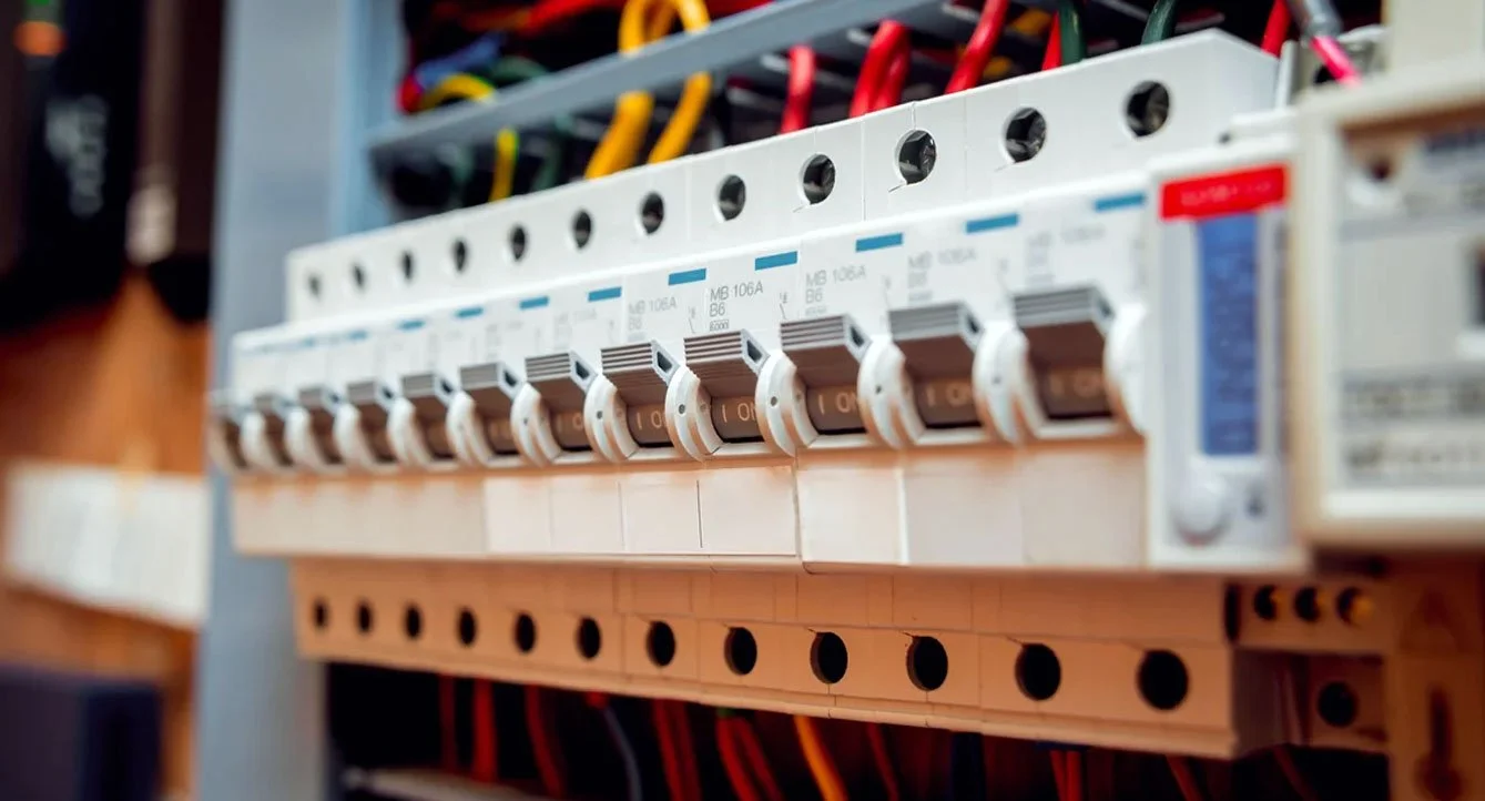Close-up of an electrical circuit breaker panel with multiple circuit breakers and colored wires.