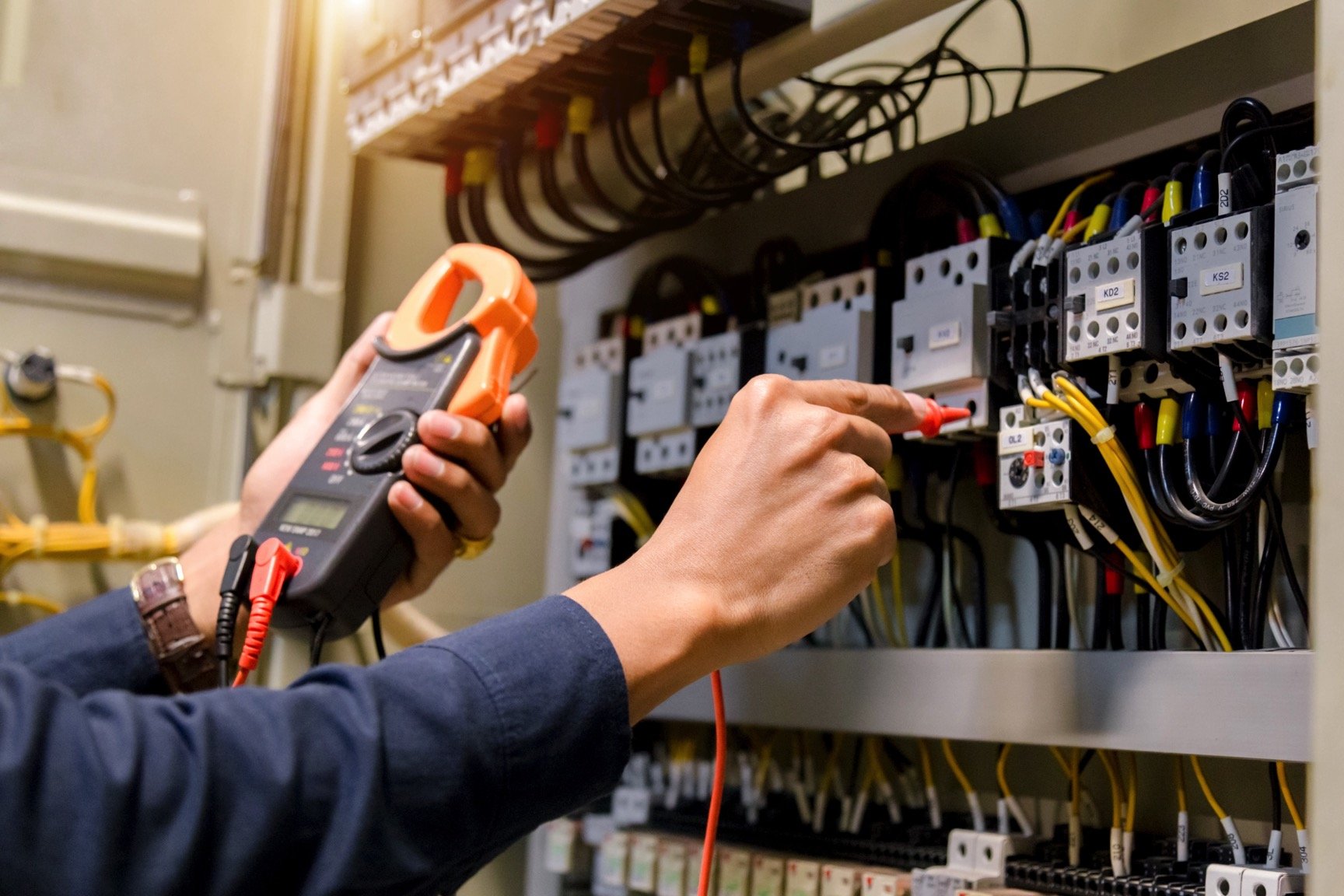 Person using a digital multimeter to test electrical wiring in an electrical panel.