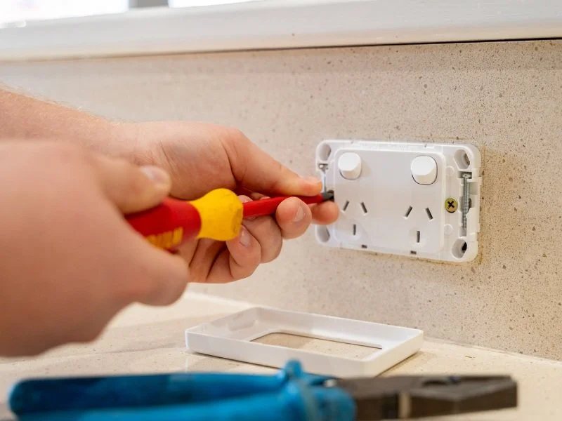 A person using a screwdriver to install or repair an electrical outlet on a wall.