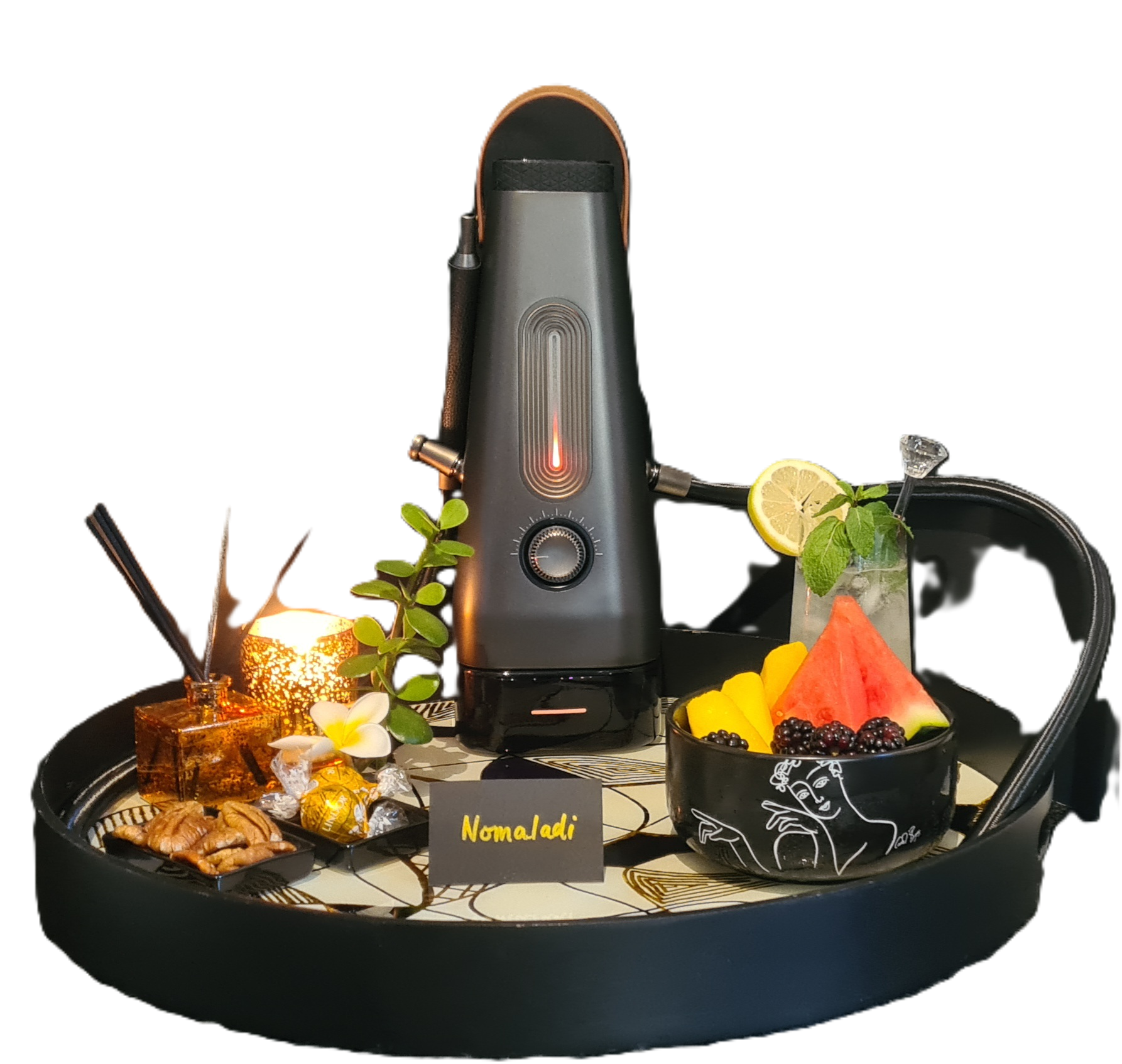A black tray with a coffee machine, various fruits including watermelon, pineapple, blackberries, and lemon slices, nuts, chocolates, and a small decorative candle in a glass holder. There is a small card labeled 'Nomad' in the center.