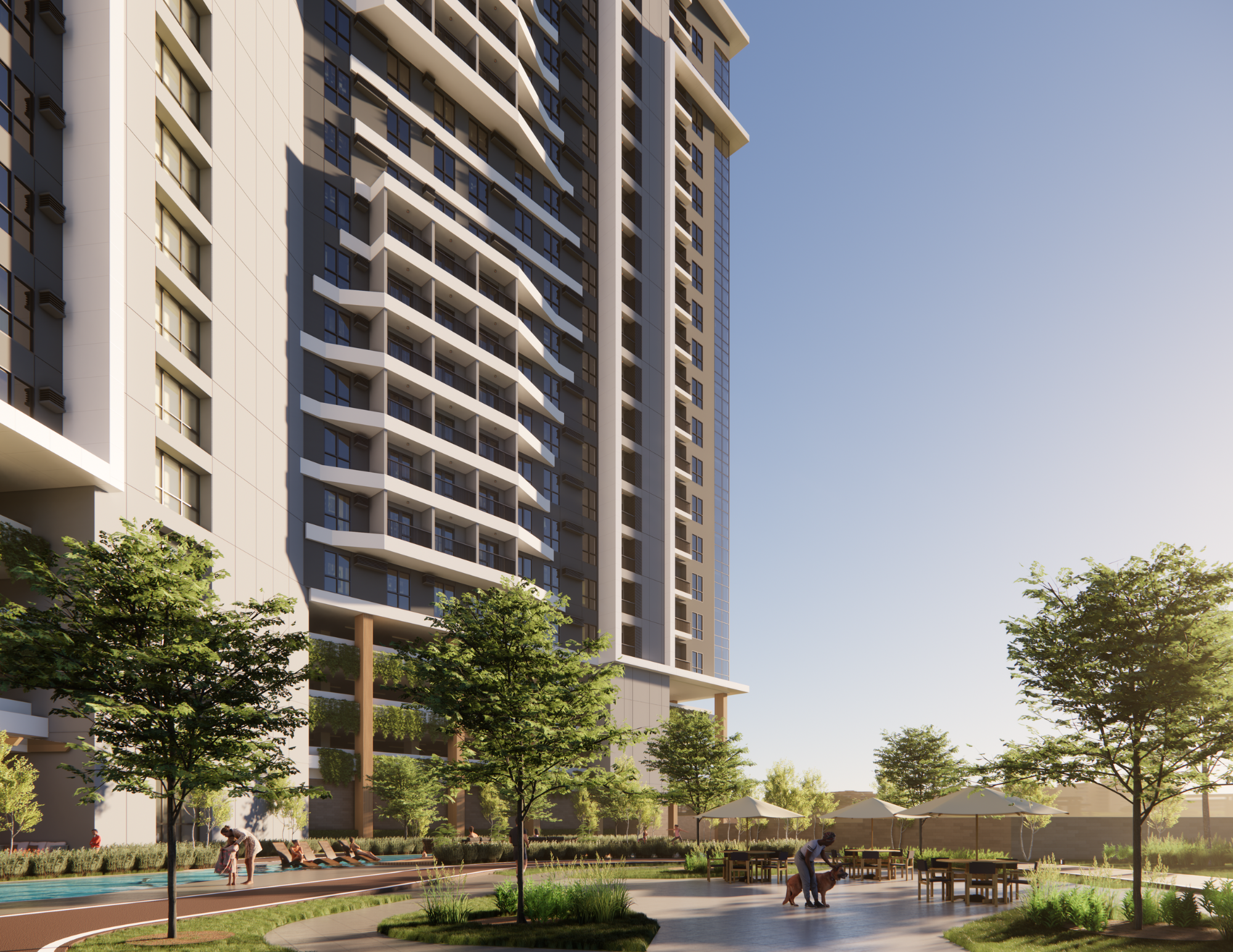 A modern high-rise apartment building with balconies, surrounding a landscaped outdoor area with trees, picnic tables under umbrellas, and a walking path. People are seen walking and relaxing.