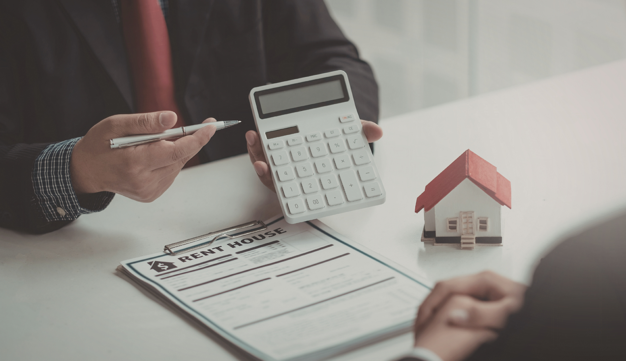 Person discussing a rent agreement with another person, holding a calculator and pen on a white table.