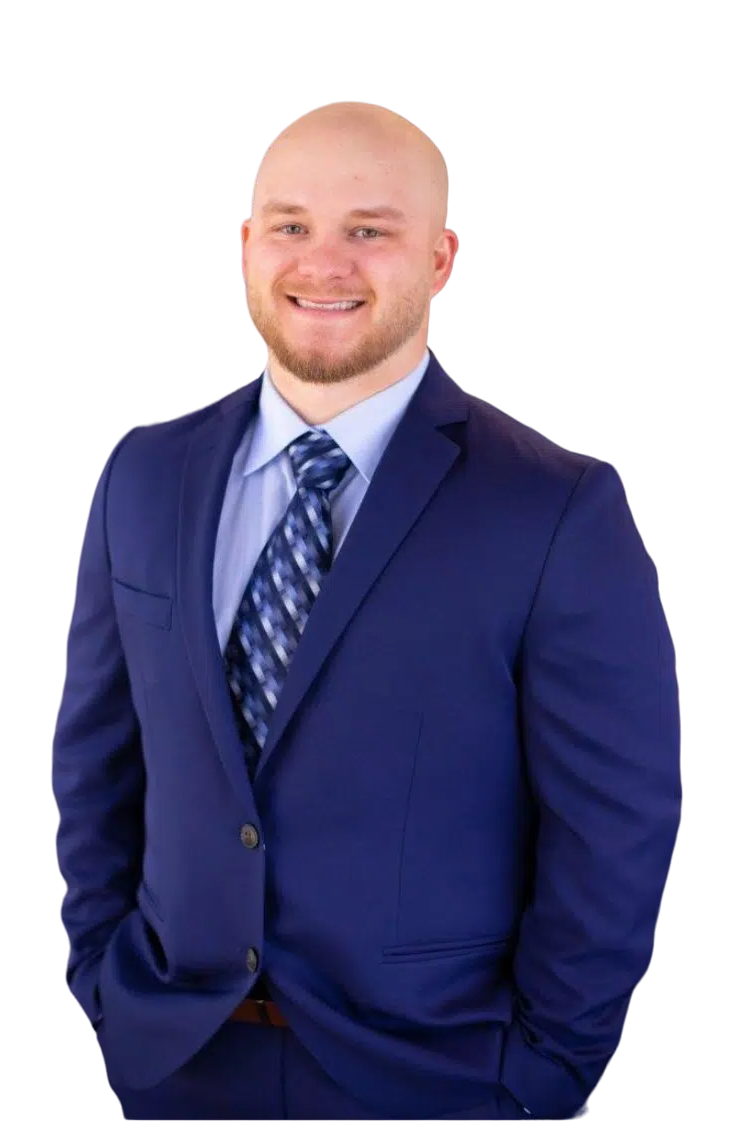 A smiling bald man with a beard wearing a navy blue suit, light blue dress shirt, and a patterned navy and light blue tie.
