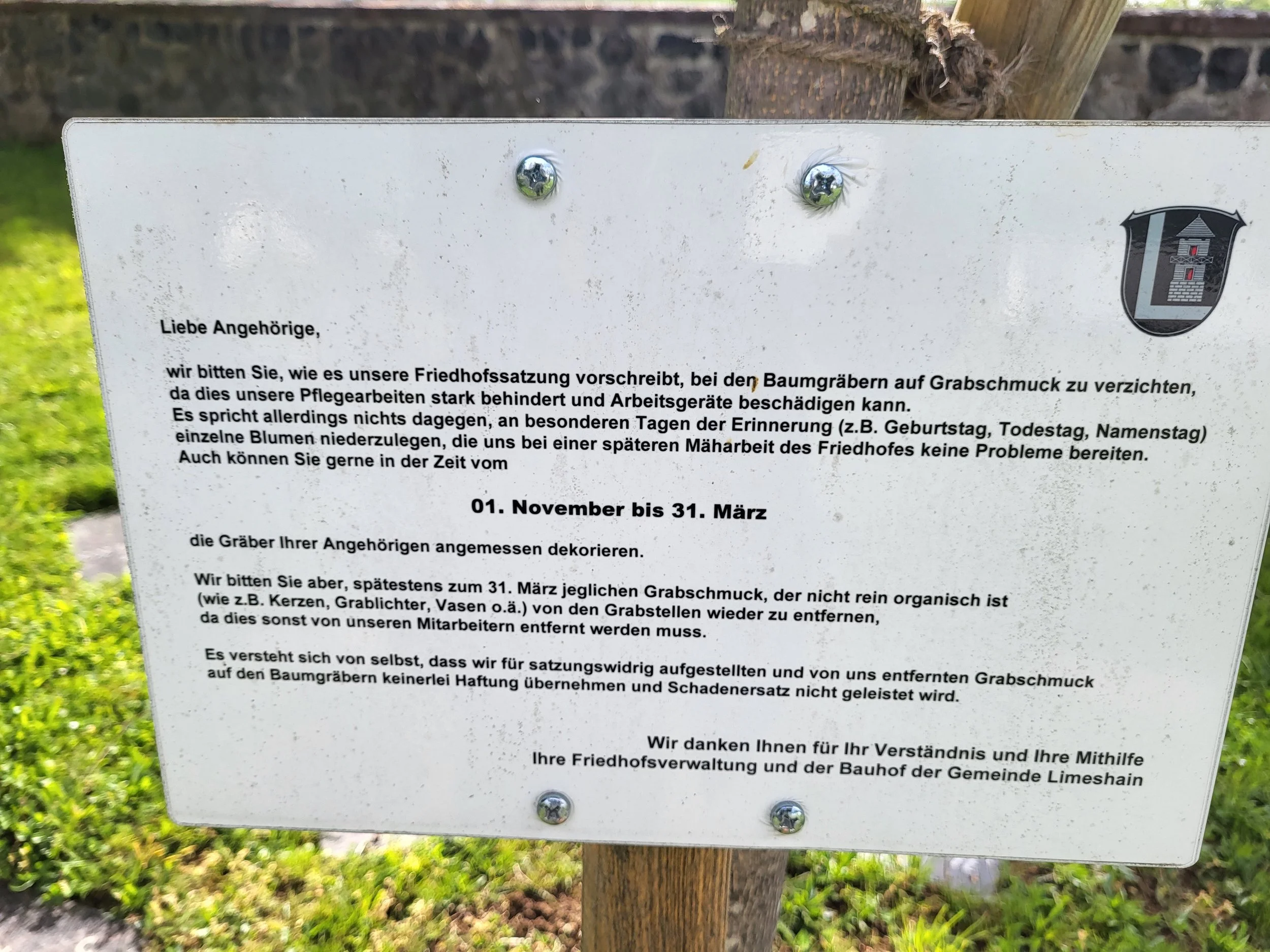 Schild mit Informationen an einem Baum im Friedhof, um das Dekorieren der Gräber während bestimmter Tage zu regeln.