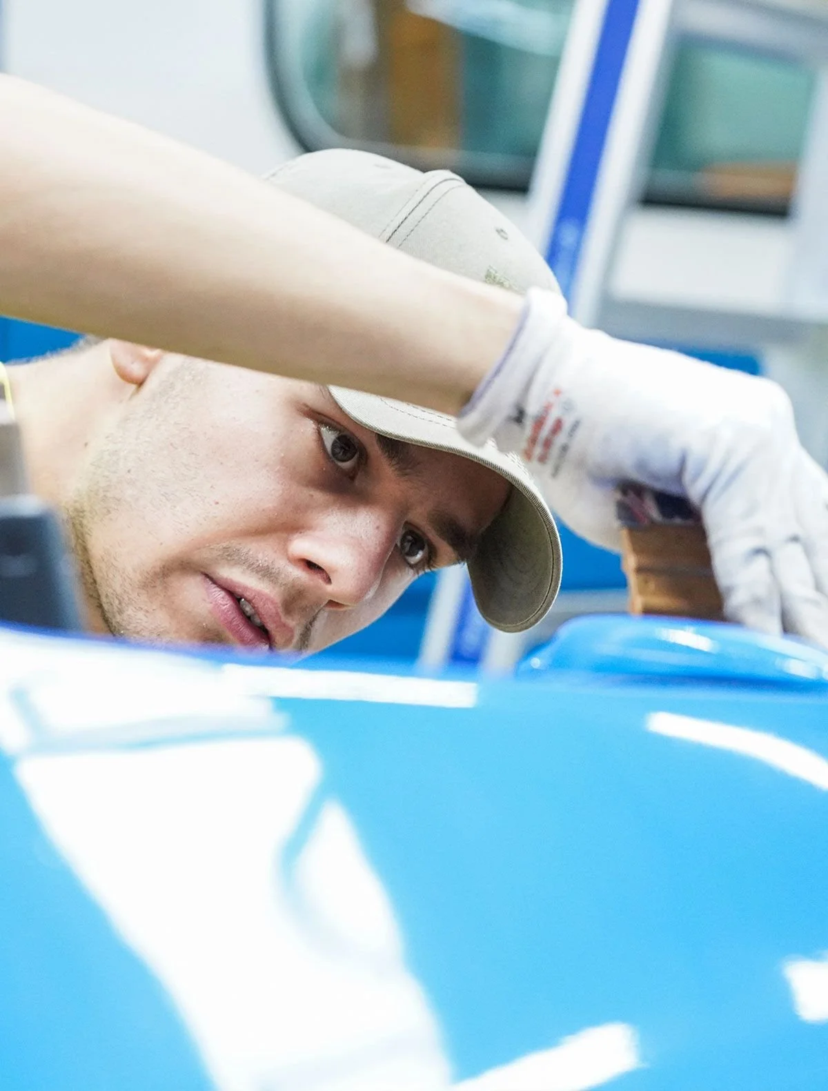 Mann arbeitet an einem Projekt, trägt einen Hut und Gummihandschuhe, und ist auf eine blaue Maschine oder ein Fahrzeug gerichtet.