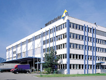 Großes modernisiertes Bürogebäude mit Glasfenstern und einer blauen Fassade, mit einem Van davor, unter einem blauen Himmel.