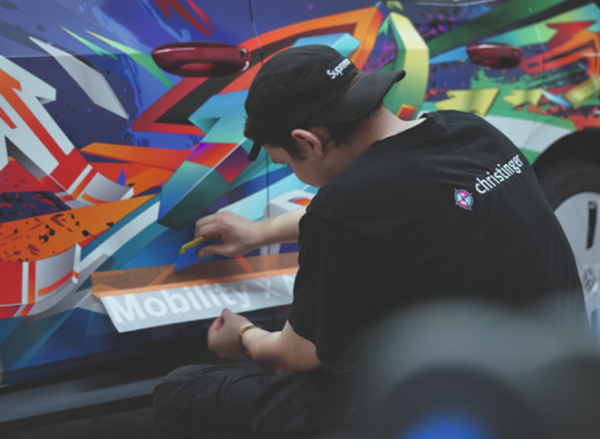 Ein junger Mann arbeitet an einem bunt bemalten Fahrzeug, das mit Graffiti-Kunst verziert ist.