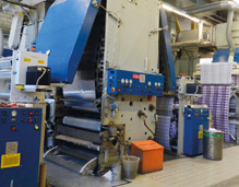 Industriemaschine in einer Fertigungsanlage, mit Rollen und Behältern im Produktionsumfeld.