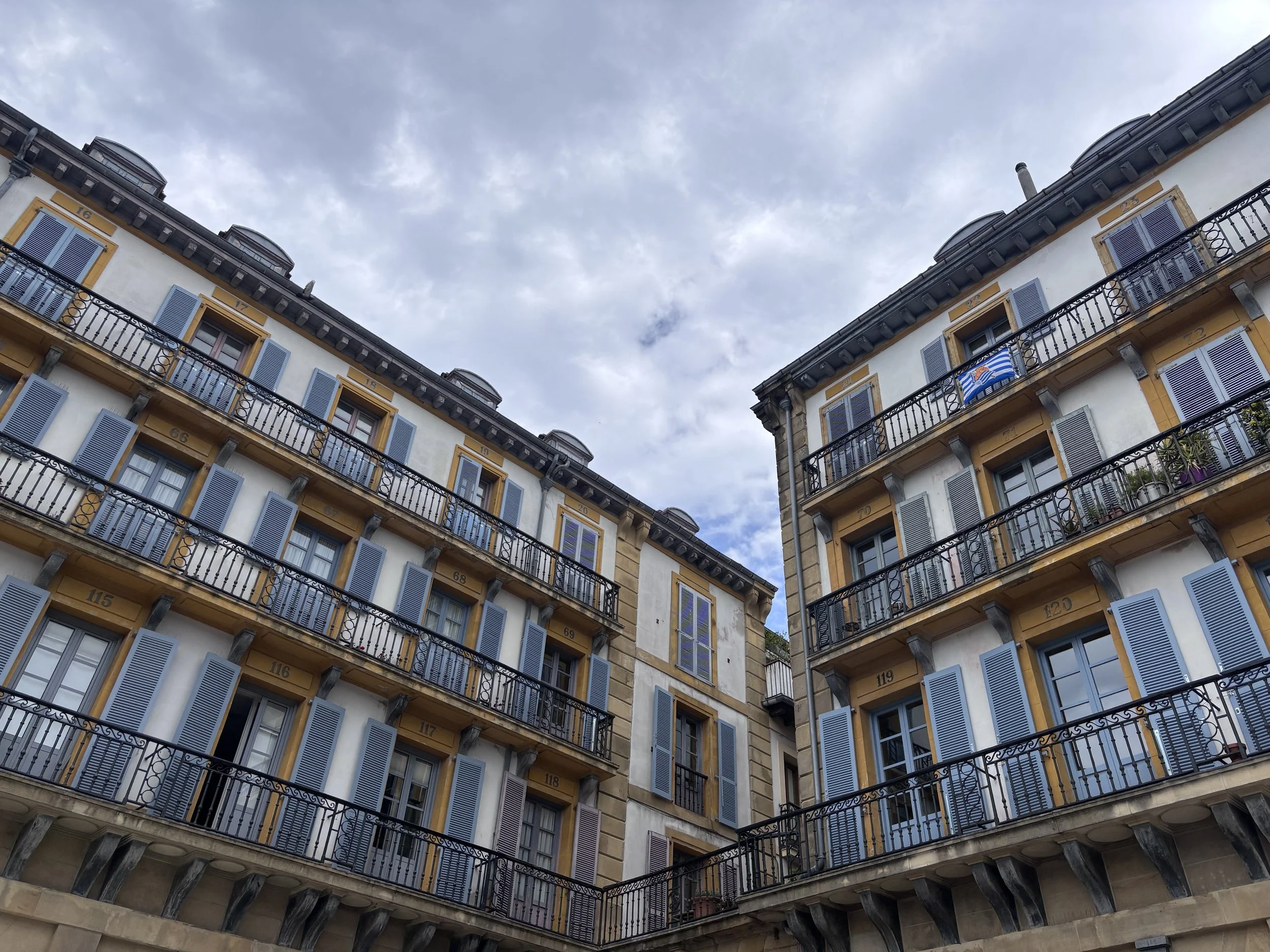 Looking up at traditional Basque architecture in San Sebastián's Old Town, featuring colorful buildings with elegant balconies and light blue shutters.