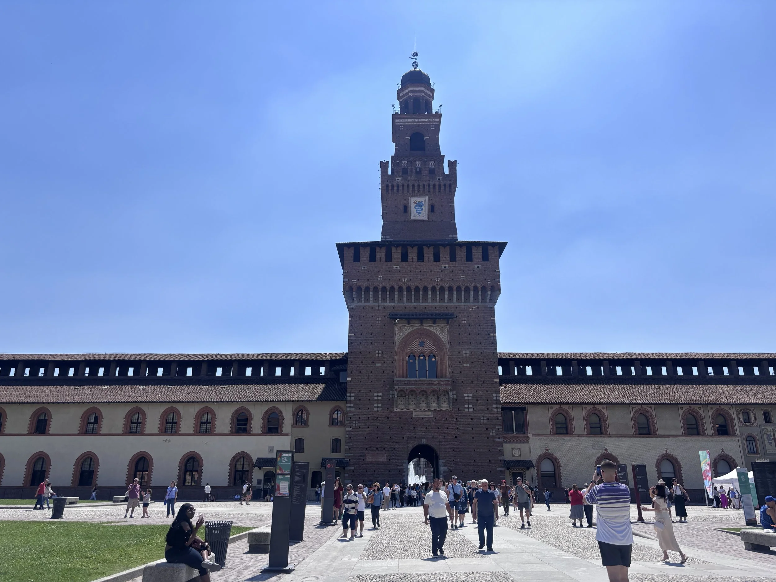 The historic Sforza Castle brick towers and fountain entrance in Milan, Italy during a bright day.