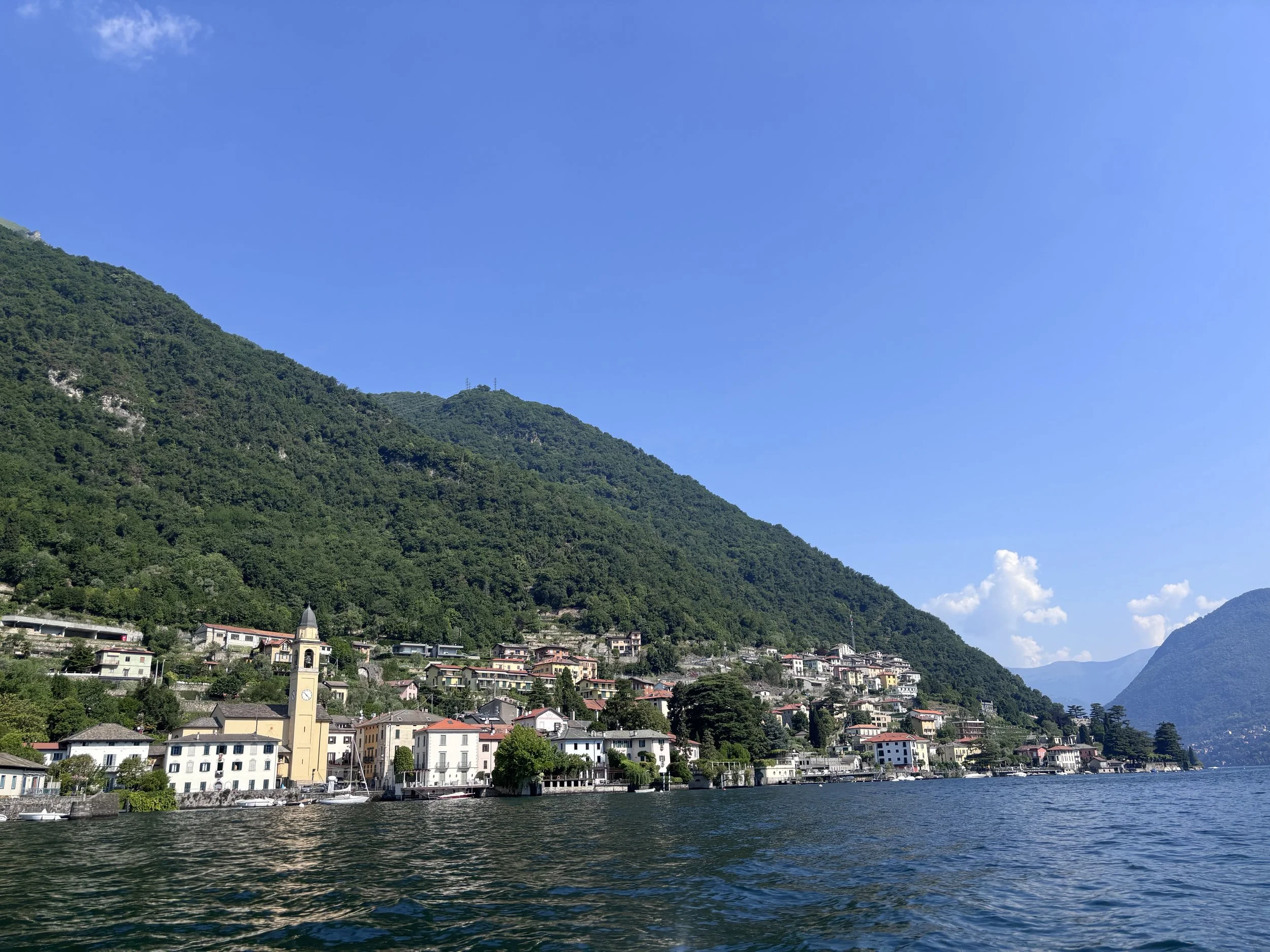 The wake of a private boat on the deep blue water of Lake Como with grand villas and mountains in the background.