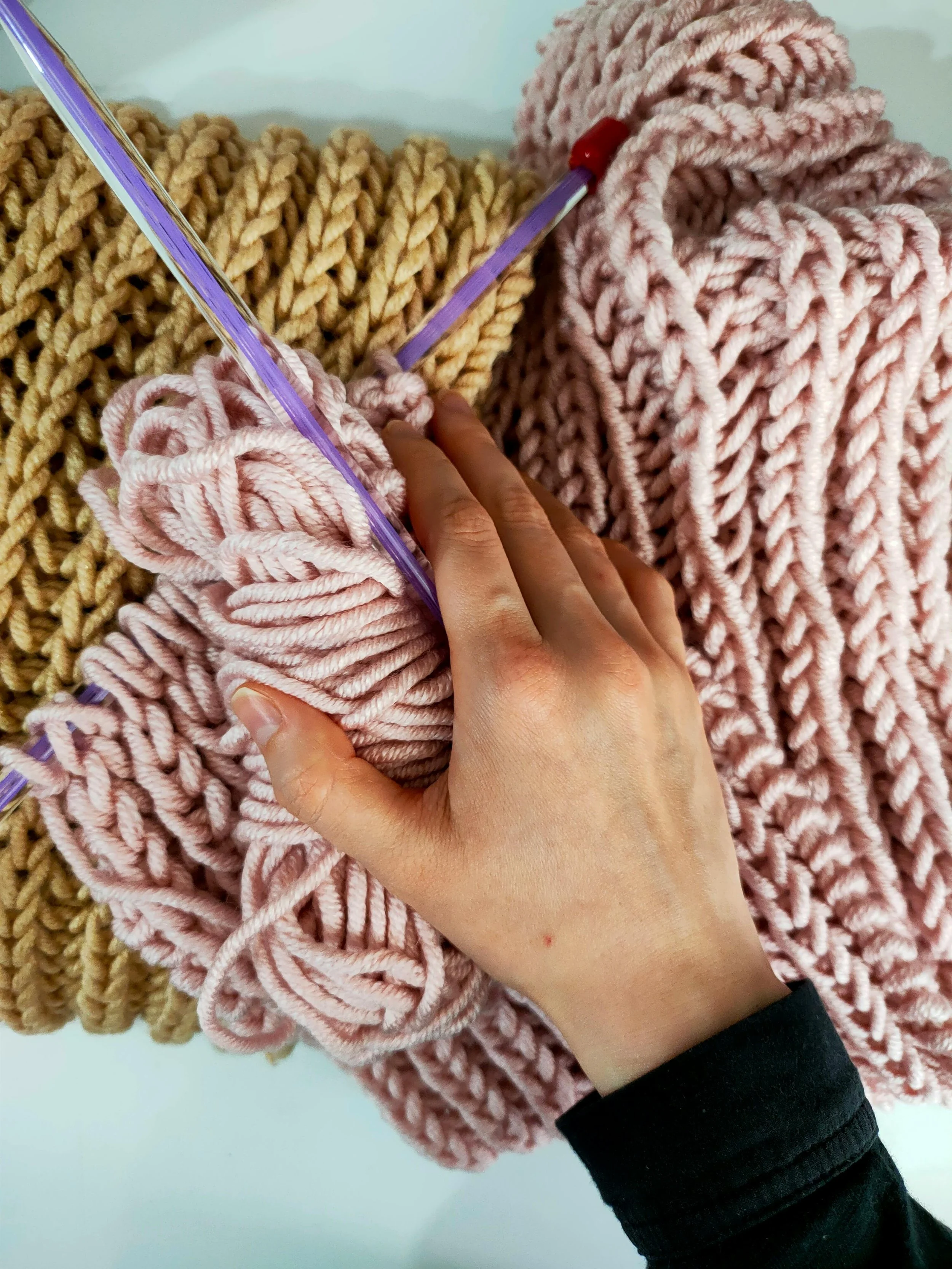 A person knitting with pink yarn, surrounded by large strands of yellow and pink yarn.