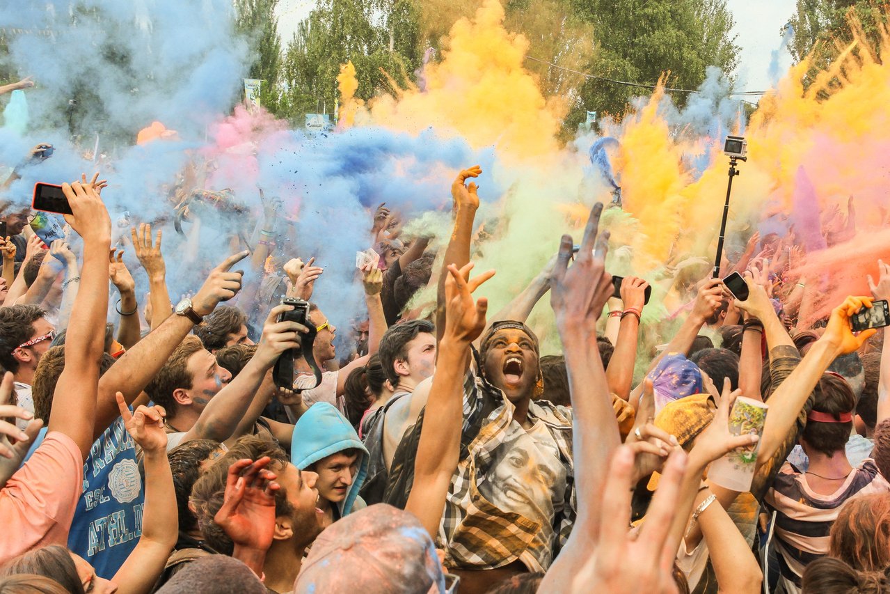 Crowd of people celebrating at a festival with color powder in the air.
