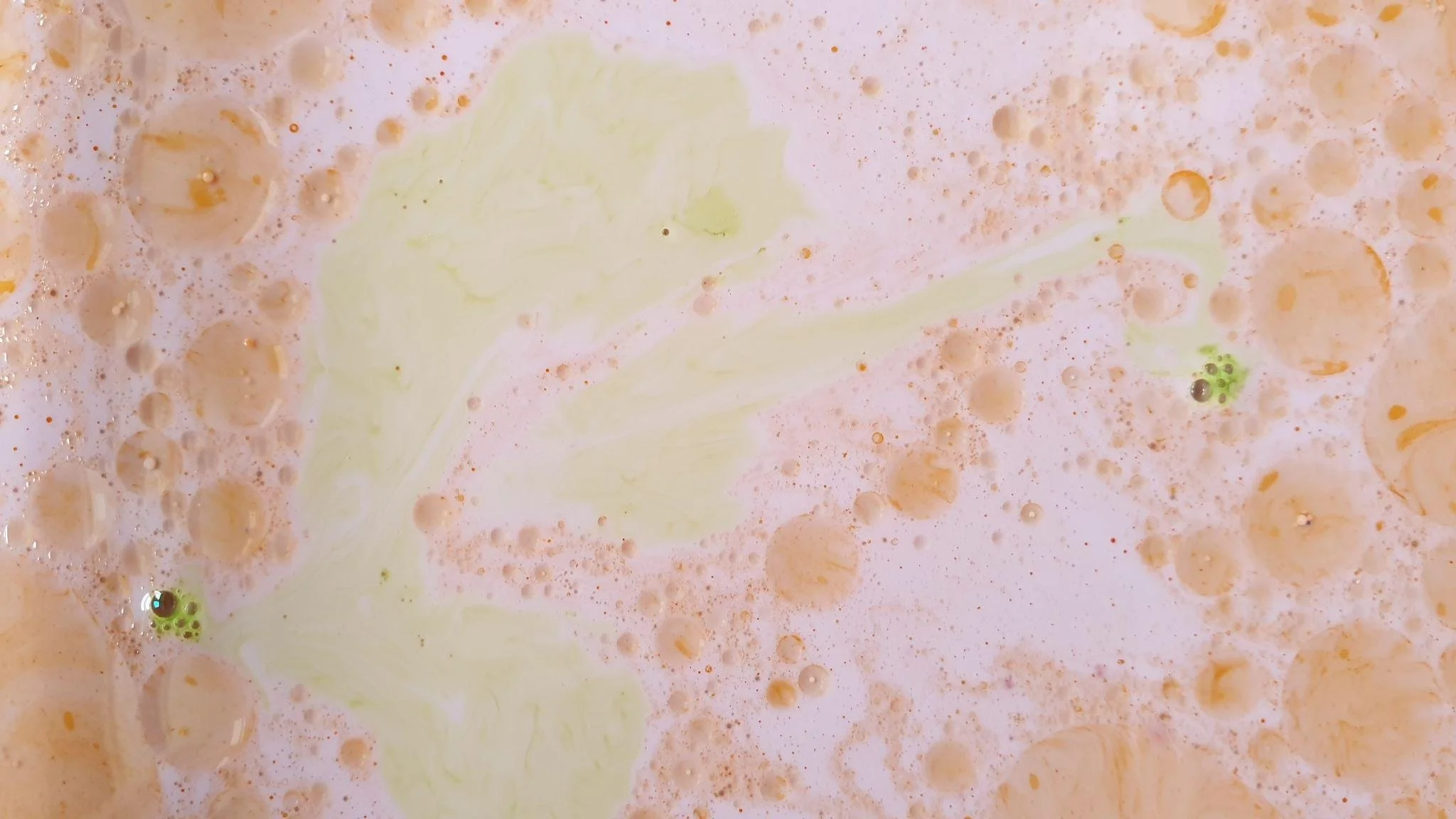 Bunte Bläschen und Schaum mit lichter, cremiger Textur in der Nähe einer hellgelben Substanz