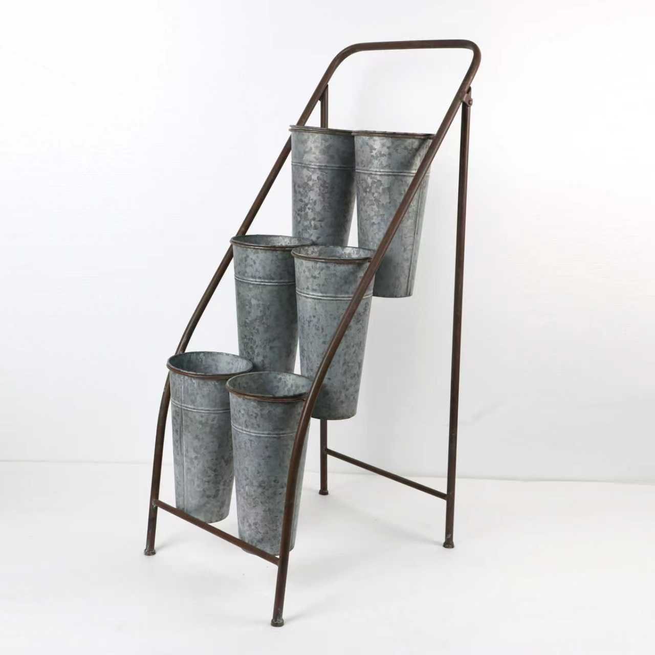 Metal outdoor plant stand with six galvanized buckets on a white background.