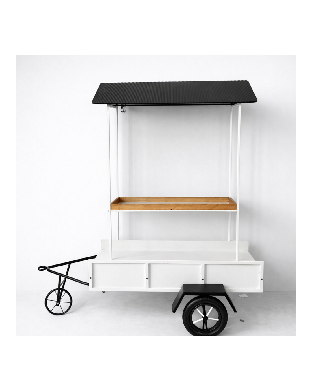 A minimalist white wooden food cart with a black roof, a brown wooden shelf, and black wheels, set against a plain white background.