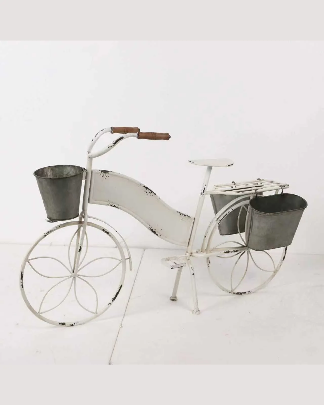 A white decorative metal bicycle with two front and back baskets, one on each side, showing signs of rust and wear.