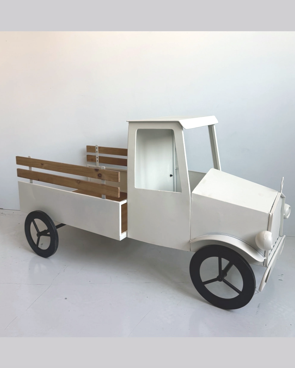 A small toy vehicle resembling a delivery truck or utility vehicle with a white body, black wheels, and wooden side panels. It appears to be a child's play vehicle or decorative item, positioned against a plain white background.