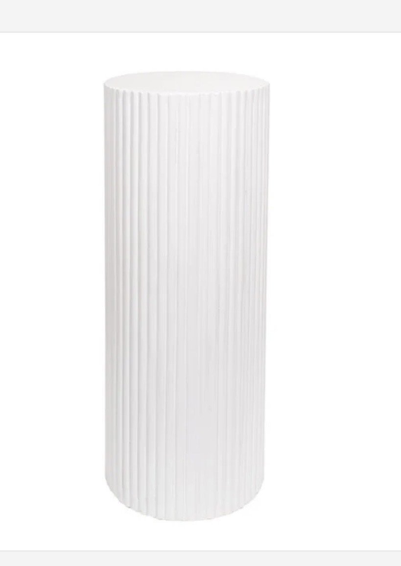 A tall white cylindrical object with vertical ridges, likely a decorative vase or container.