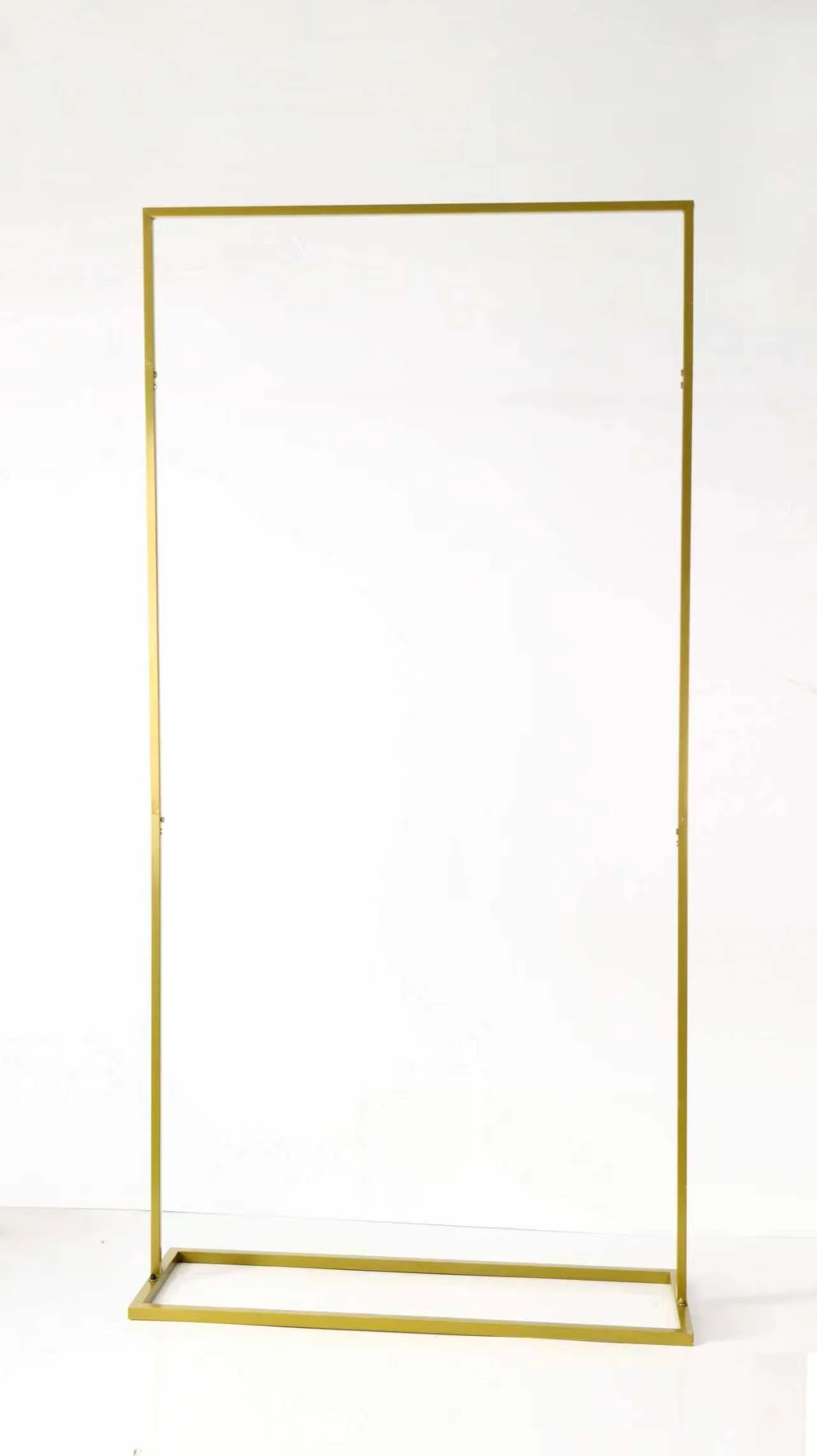 A gold-colored metal clothing rack with no clothes, standing on a white floor and against a plain white background.