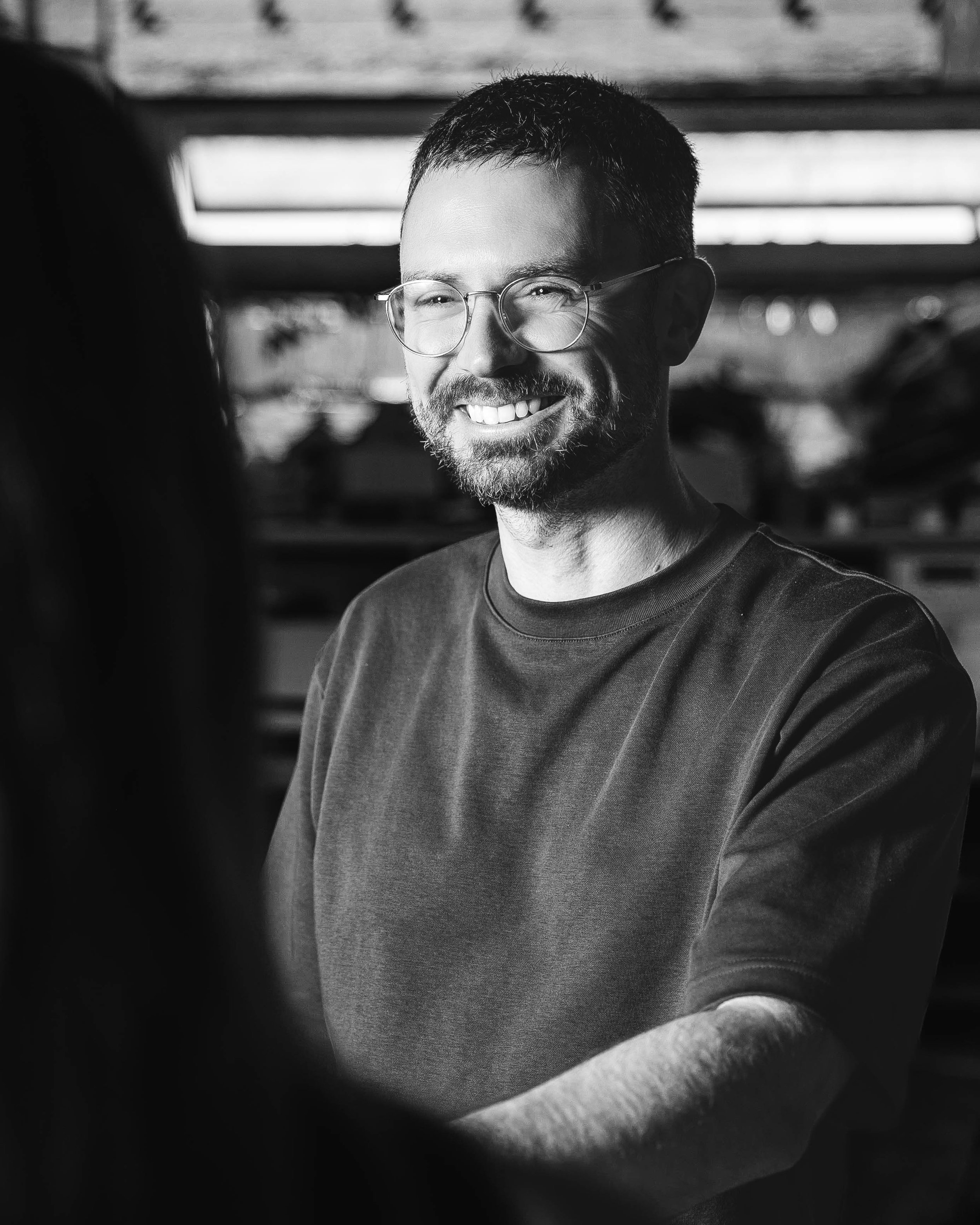 A smiling man with glasses and a beard. Black-and-white photo, background blurred.