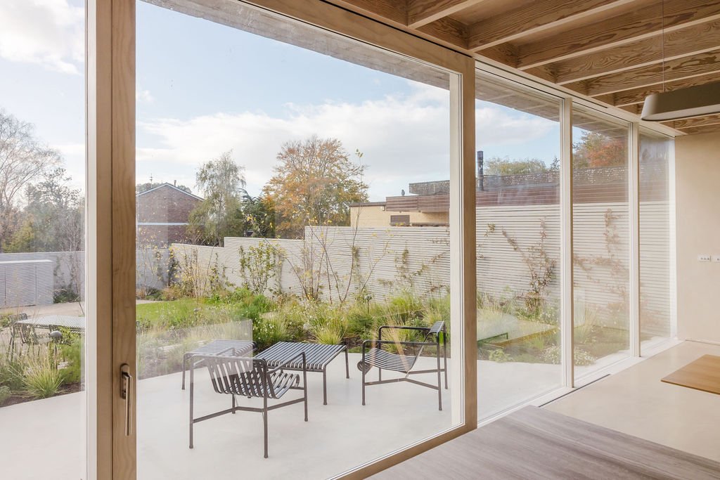 View of a backyard garden through large sliding glass doors, featuring outdoor chairs and plants.