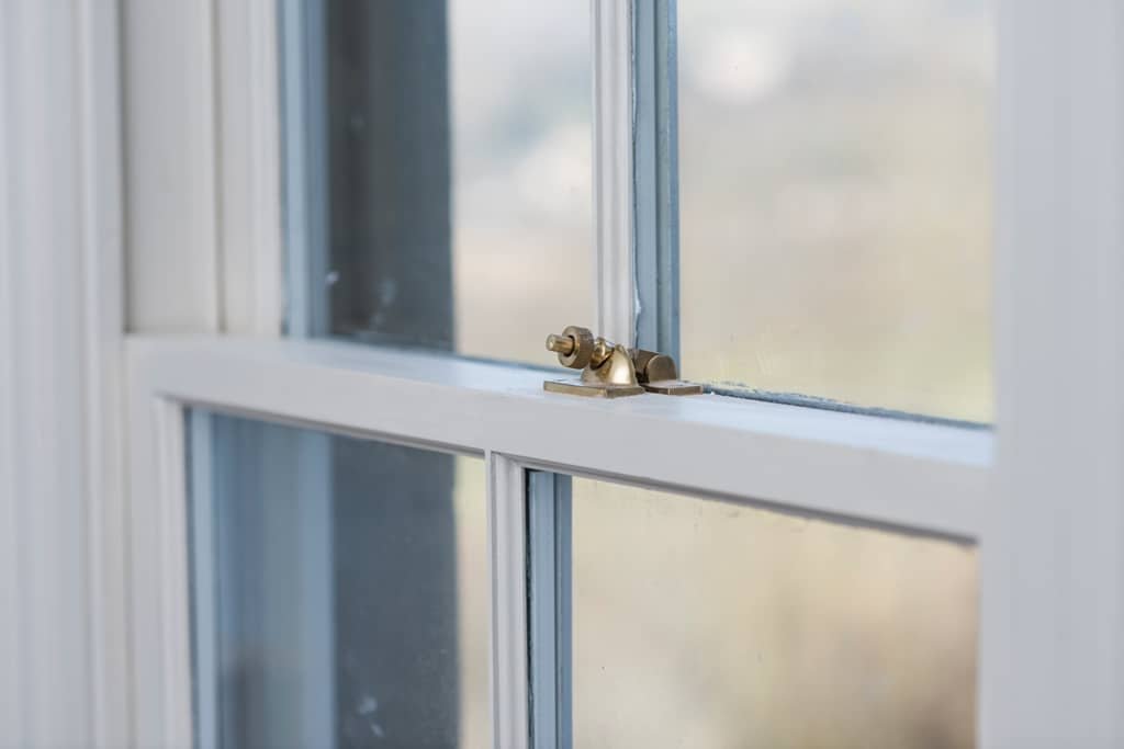 Close-up of a brass window latch on a white-framed window with clear glass panes.