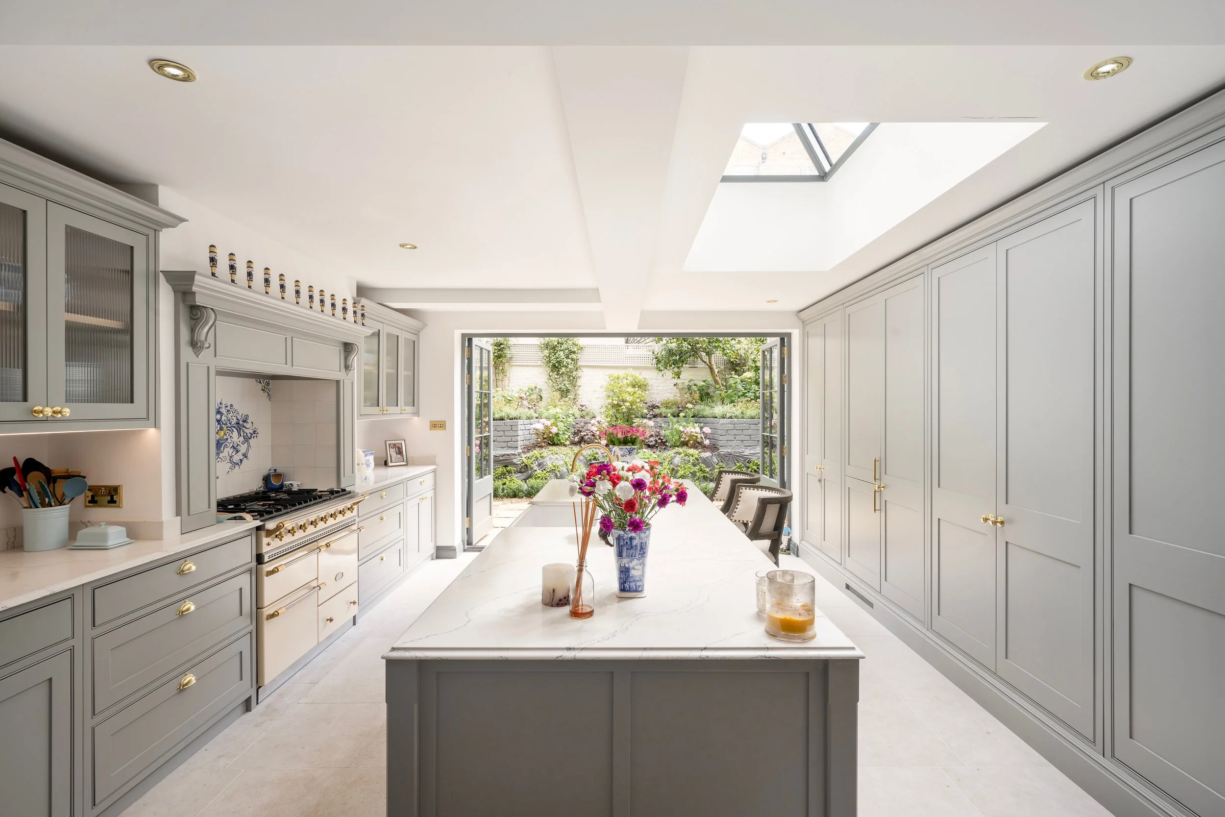 Bright kitchen with white cabinets, a large island, and an open door leading to a garden patio with flowers and trees.