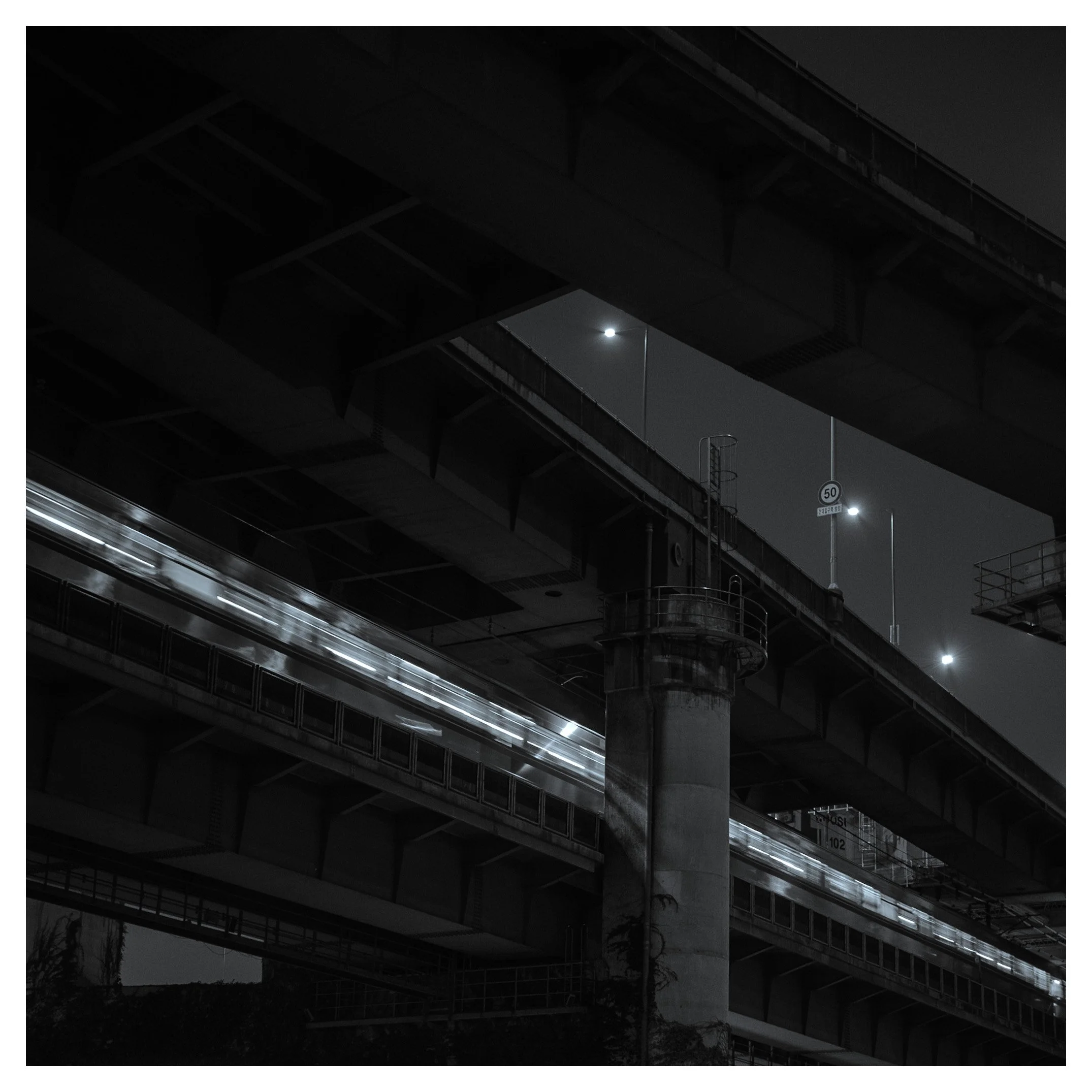 Nighttime view of multiple overlapping highway overpasses with a blurred train passing underneath, illuminated streetlights, and a dark sky with a bright full moon.