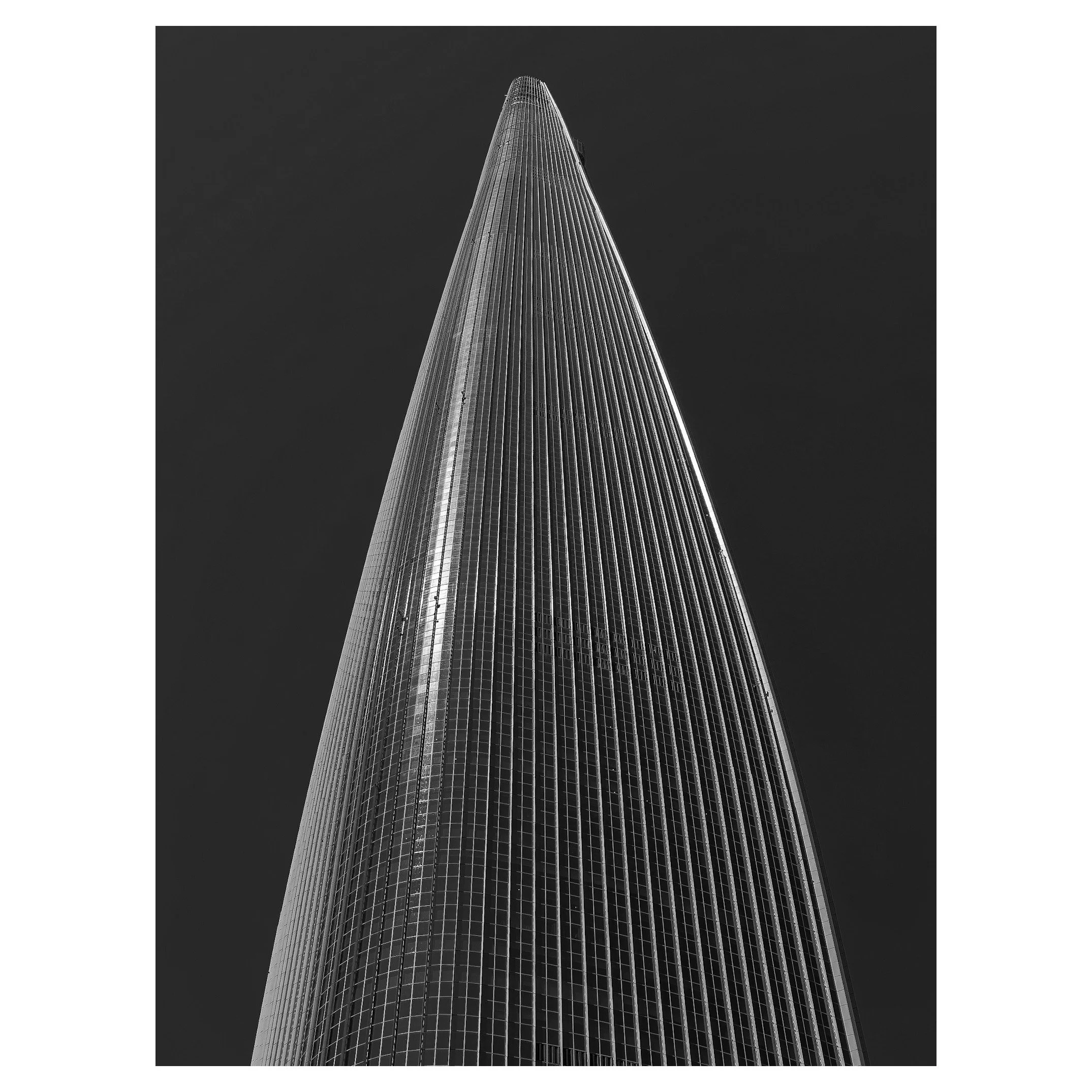 A black-and-white photo of a tall skyscraper taken from the ground looking up, emphasizing its height and sleek design.