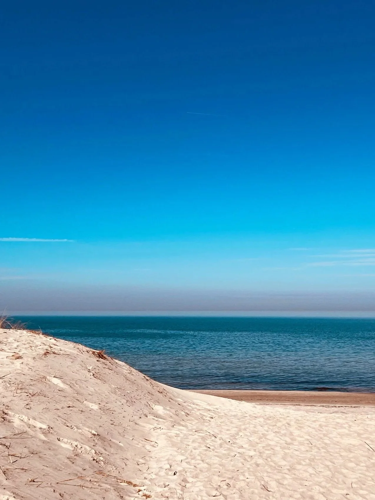 Blick über eine Sanddünen auf das Meer darüber der blaue Himmel. Strand Motiv in Graal Müritz.