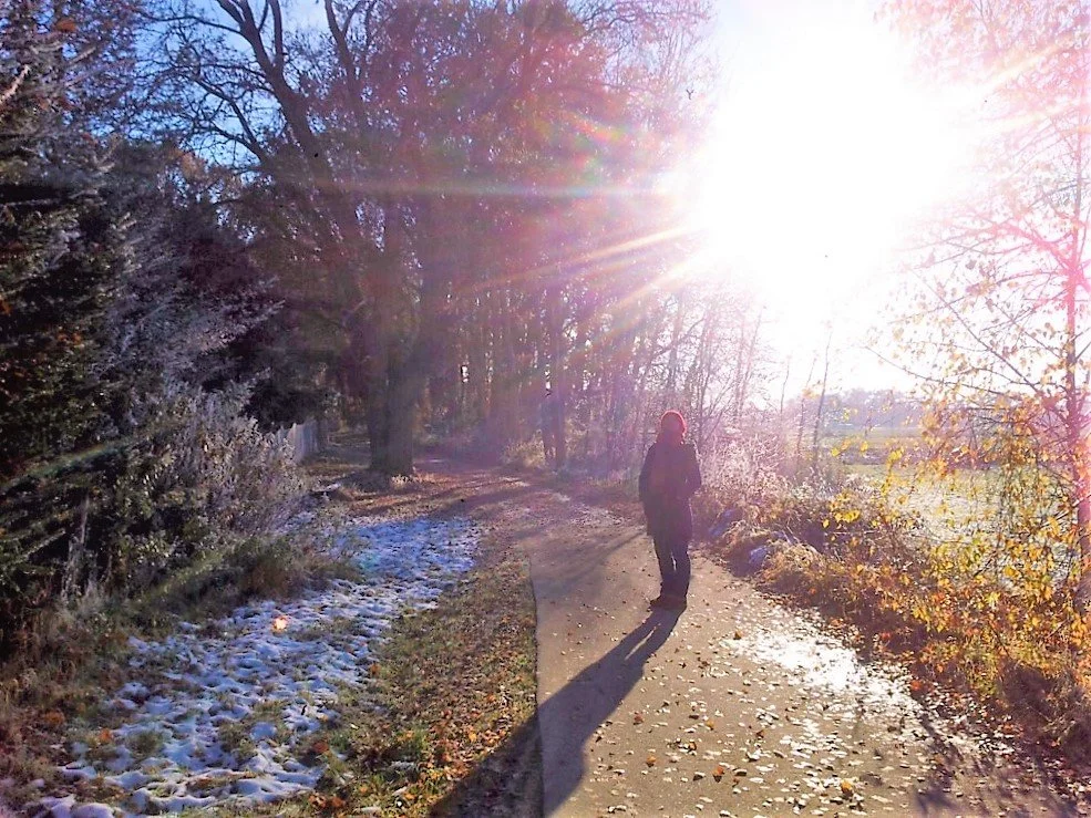 Eine entspannte Person steht auf einem Weg in einer winterlichen sonnigen Landschaft