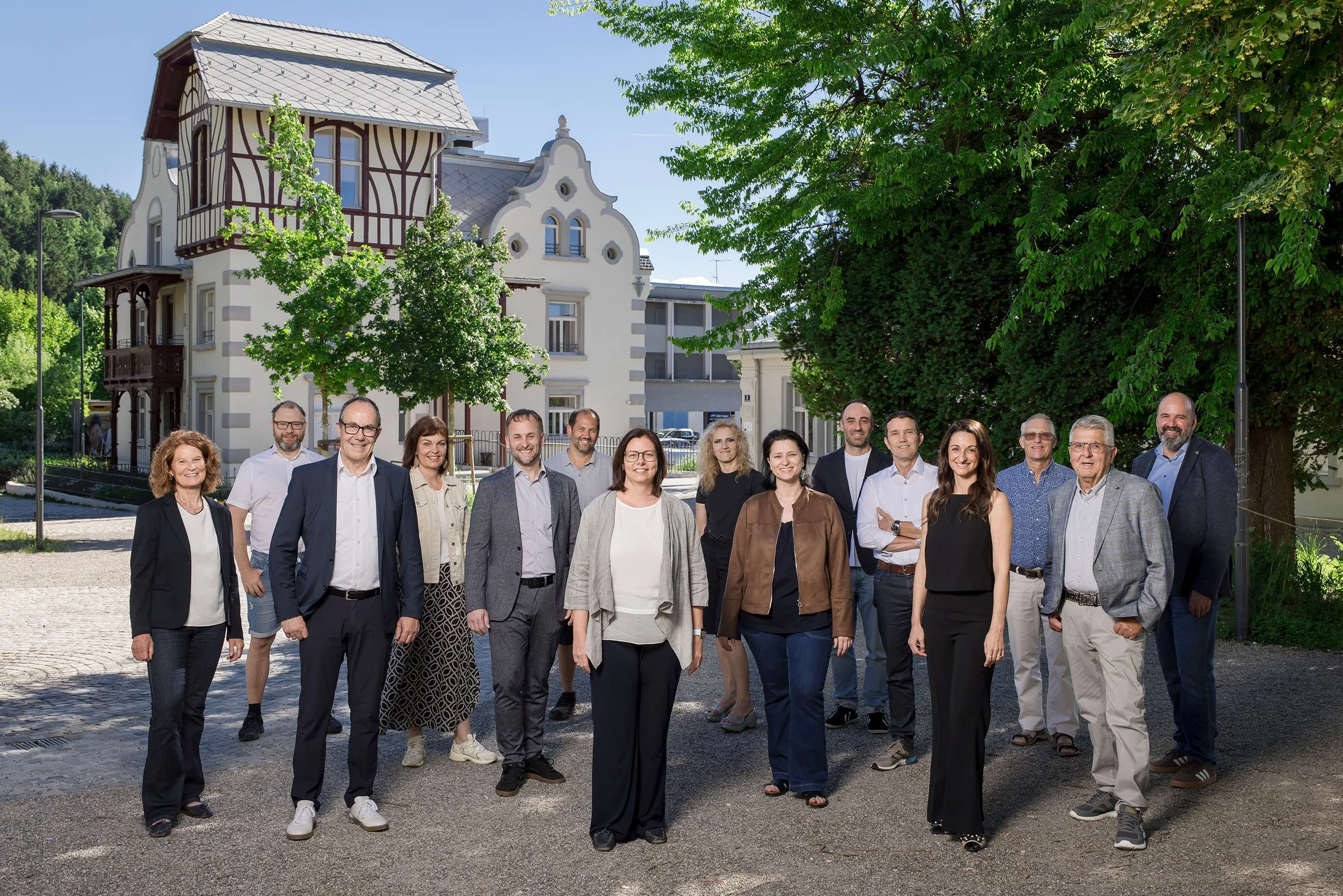 Die Mitglieder der Volkspartei Rankweil stehen auf einer gepflasterten Straße von der Häusle Villa in Rankweil, umgeben von grünen Bäumen an einem sonnigen Tag.