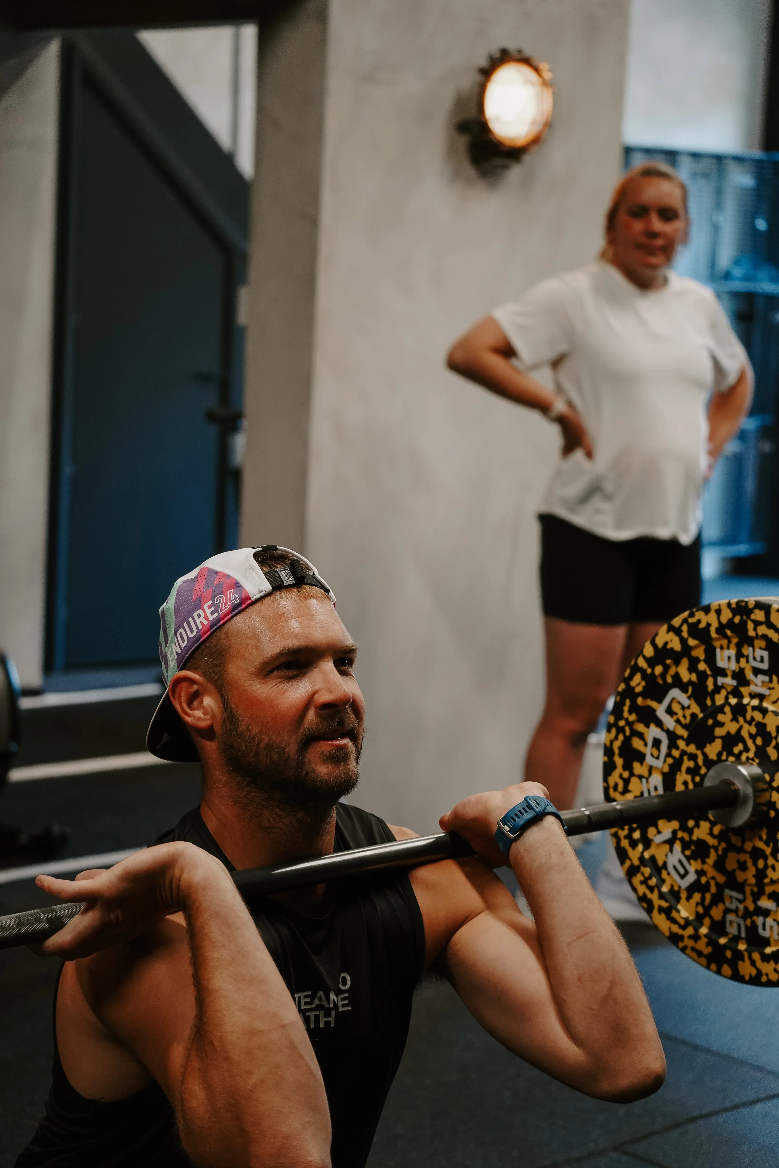 Man smiling while performing a barbell front squat in a gym.