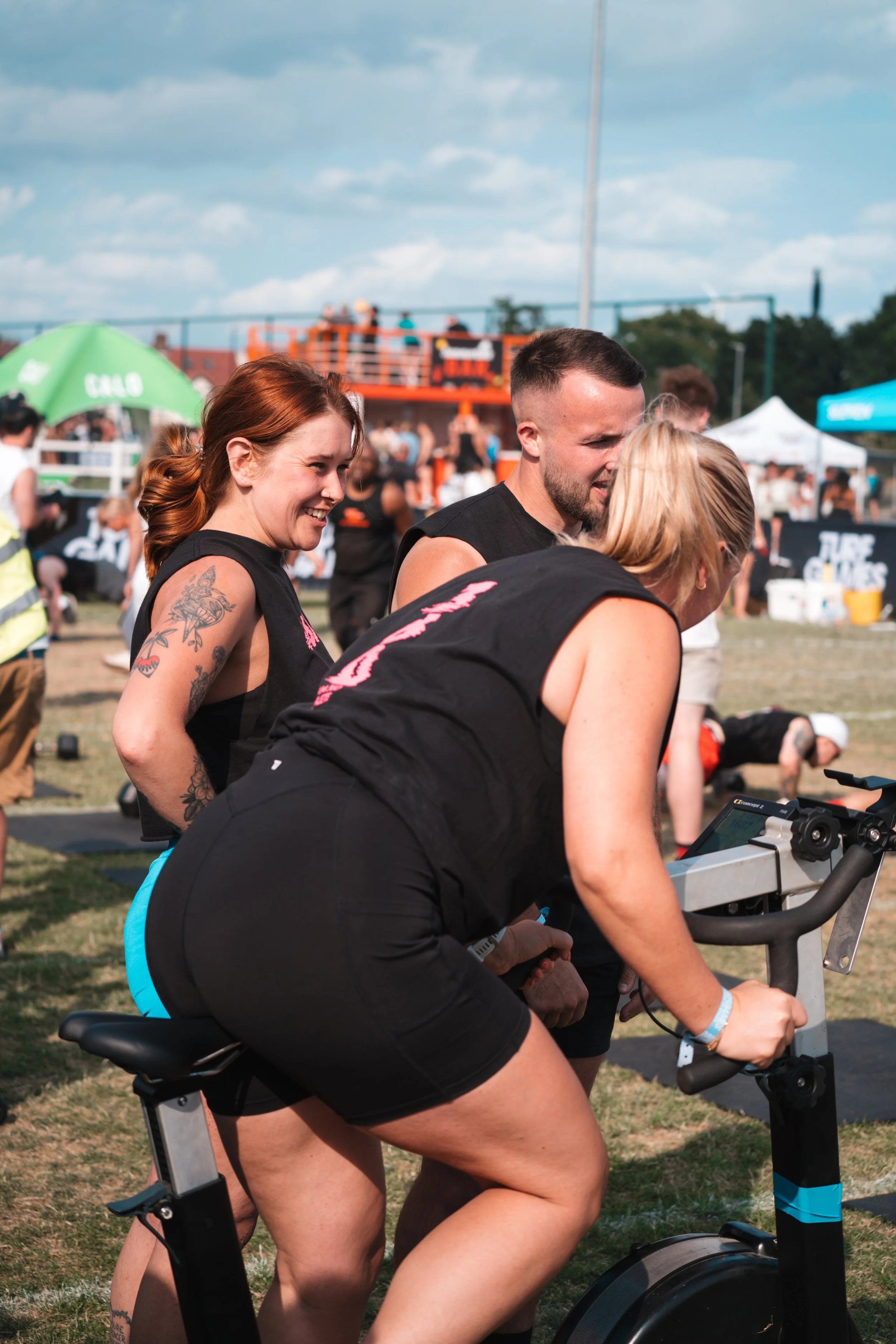 Group of members competing in a turf fitness game, with a woman riding an air bike.